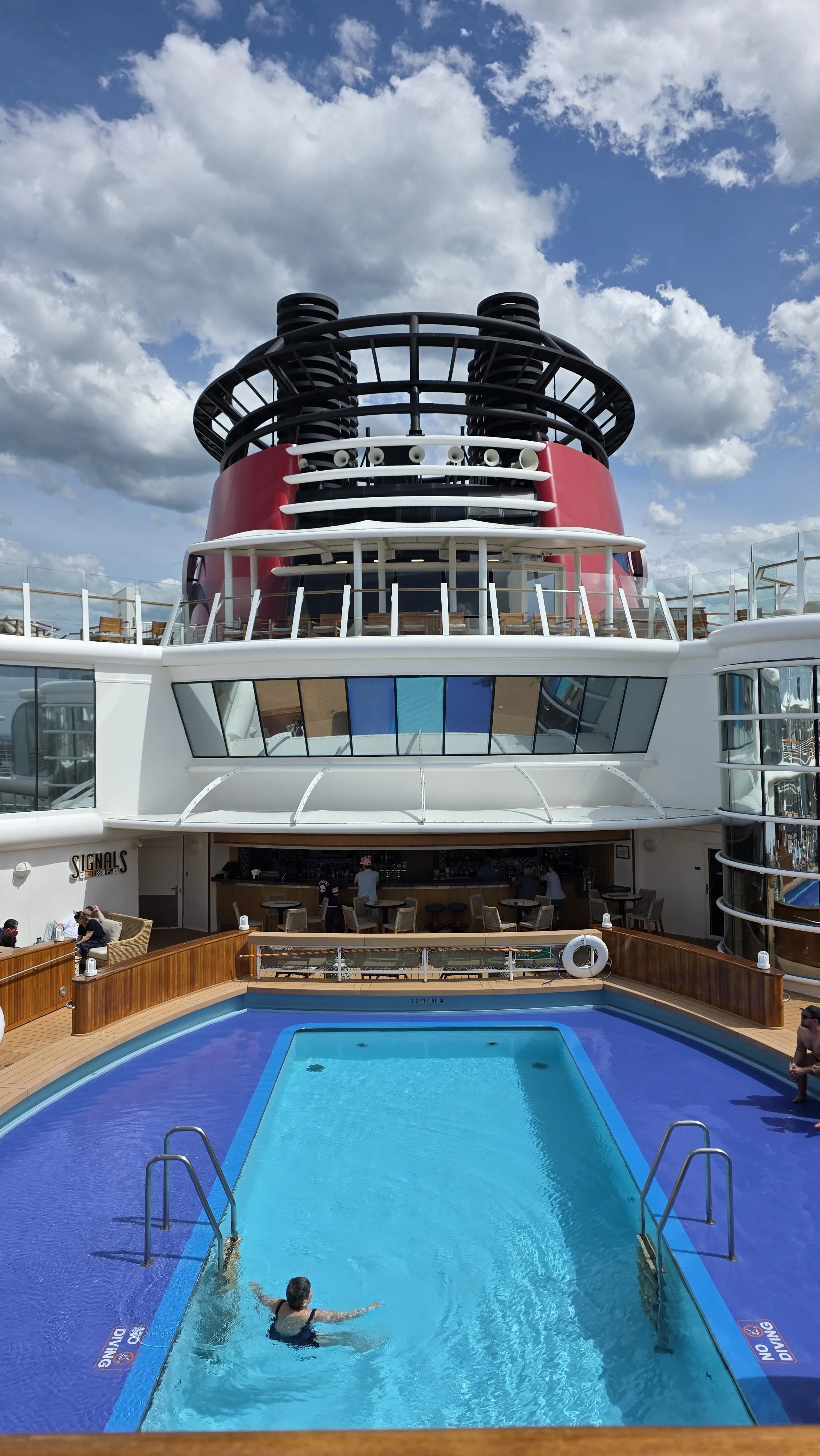 A person swimming in a pool on a cruise ship with the ocean and a partly cloudy sky in the background.