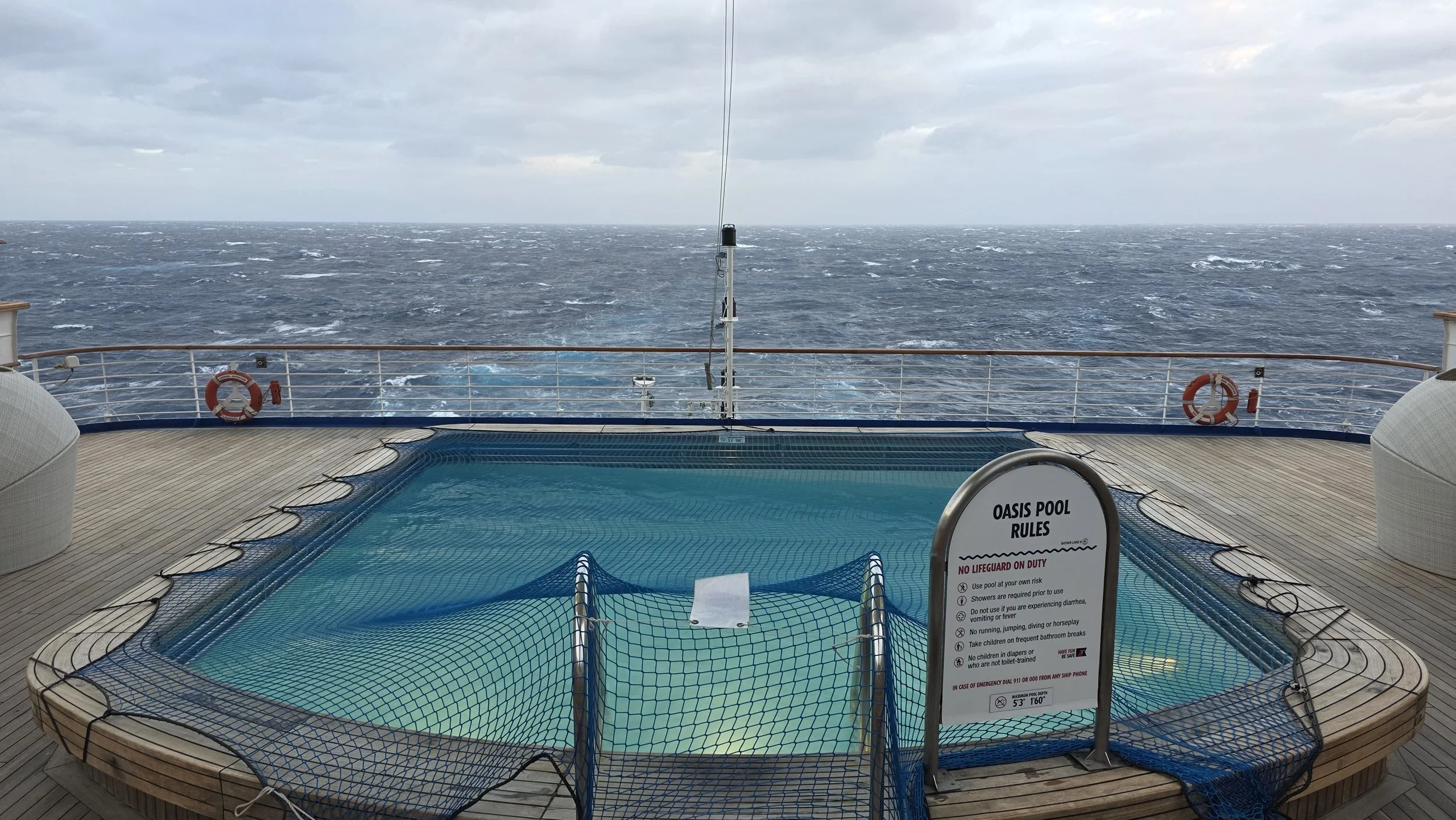 A small pool on the deck of a cruise ship with a view of the open ocean and a cloudy sky in the background.