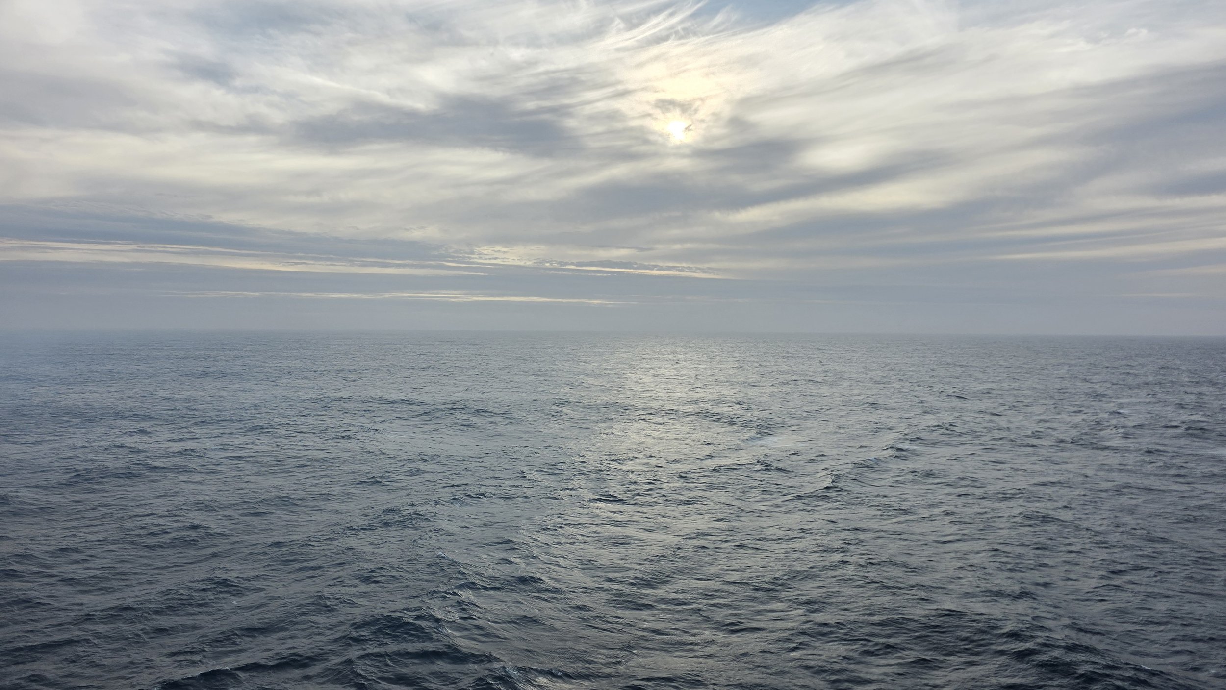 Image of a calm ocean with a cloudy sky and the sun partially obscured.