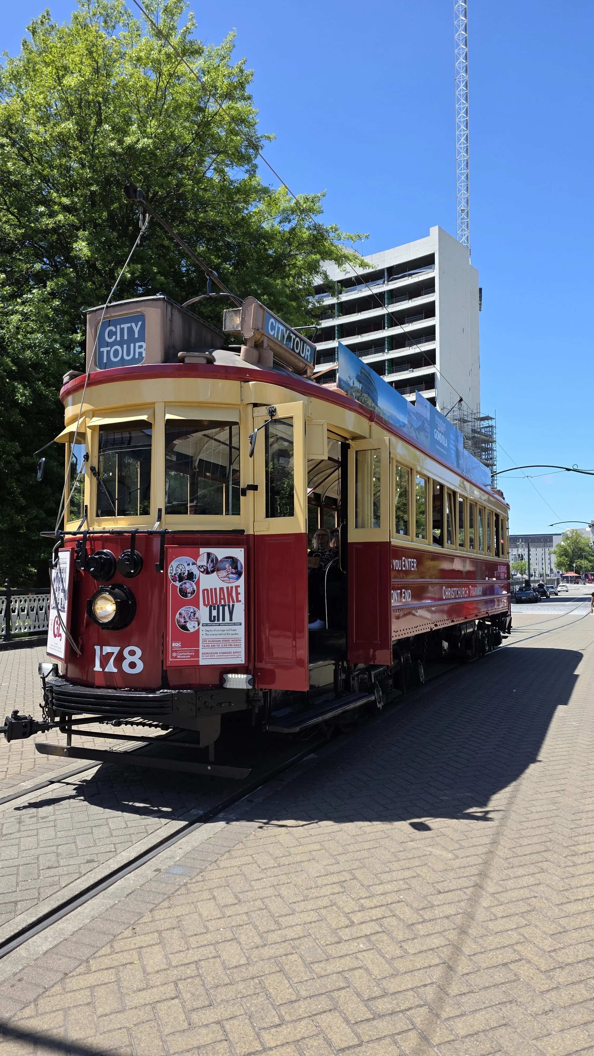 Red and yellow vintage trolley car on tracks with city tour advertisements and a sign for Quake City in San Francisco, with modern buildings and a blue sky in the background.
