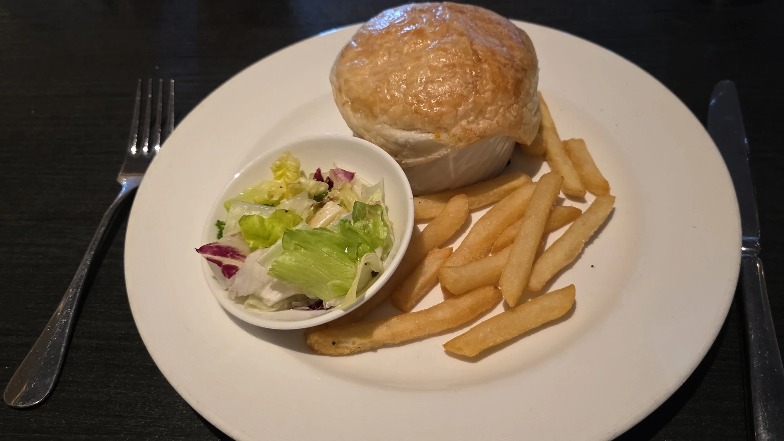 A plate with a baked potato topped with cheese, French fries, and a side salad with lettuce and radicchio, seen with silverware on either side.