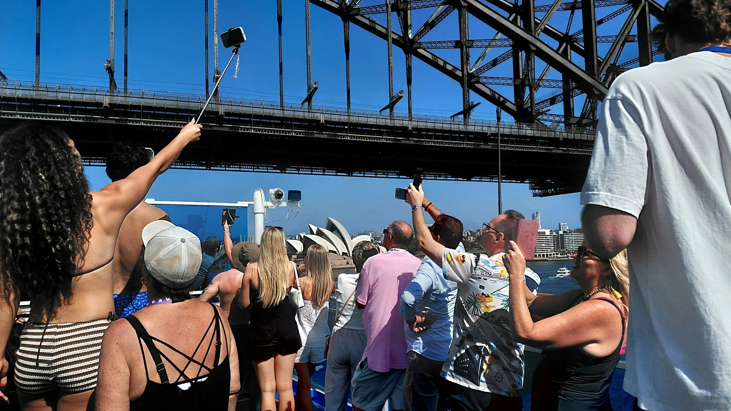 People on a boat taking photos of the Sydney Opera House and Harbour Bridge with smartphones and tablets during the daytime.