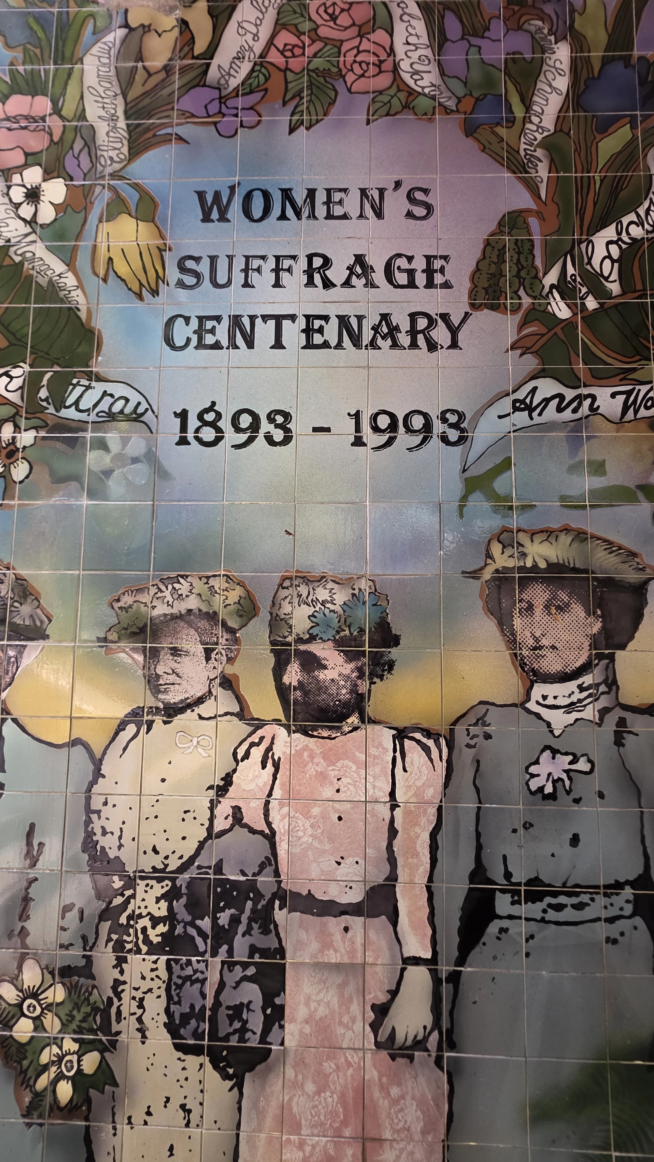 A commemorative tile mural celebrating the Women's Suffrage Centenary from 1893 to 1993, featuring images of three women in vintage clothing, surrounded by floral designs and inscriptions.