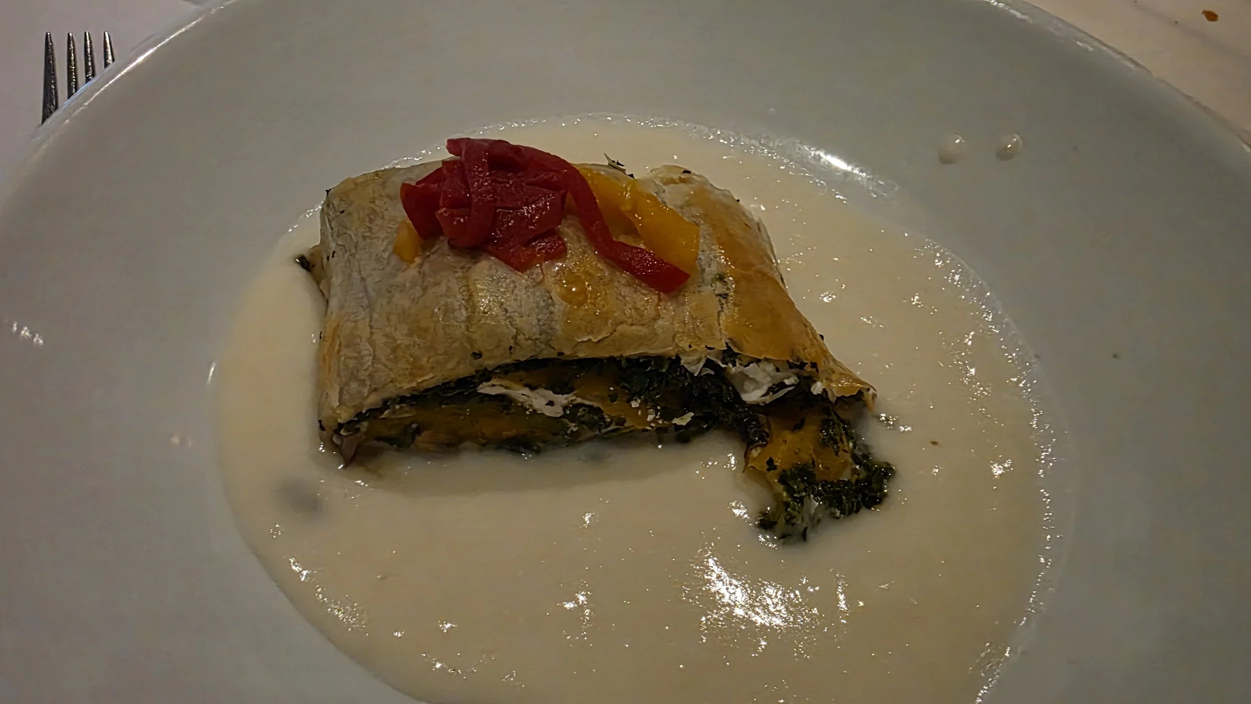 A serving of stuffed eggplant with a creamy white sauce and red and yellow bell peppers on top, on a white plate.