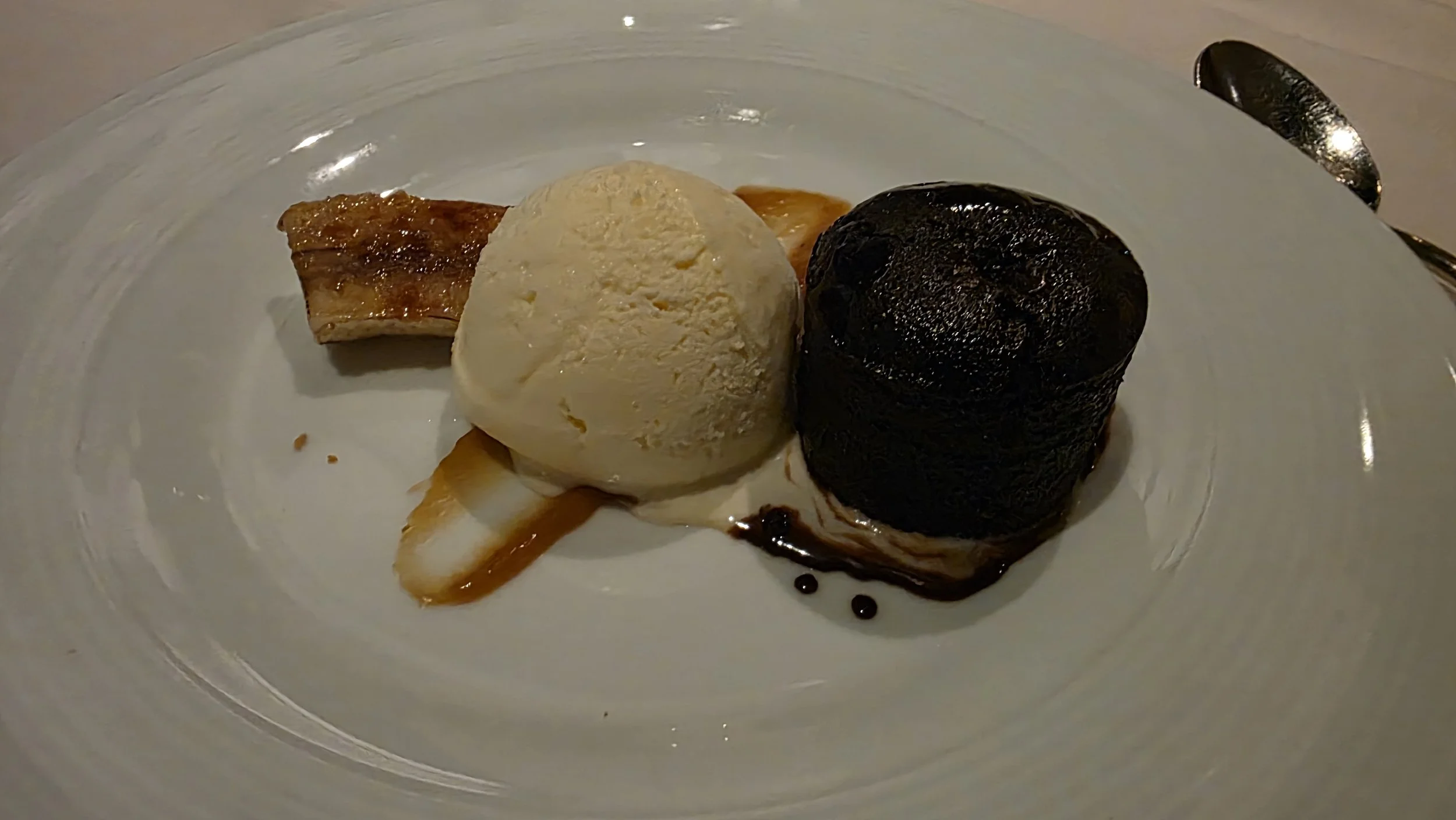 Dessert plate with a scoop of vanilla ice cream, a baked apple, and a small chocolate roulade, garnished with caramel sauce and chocolate sauce