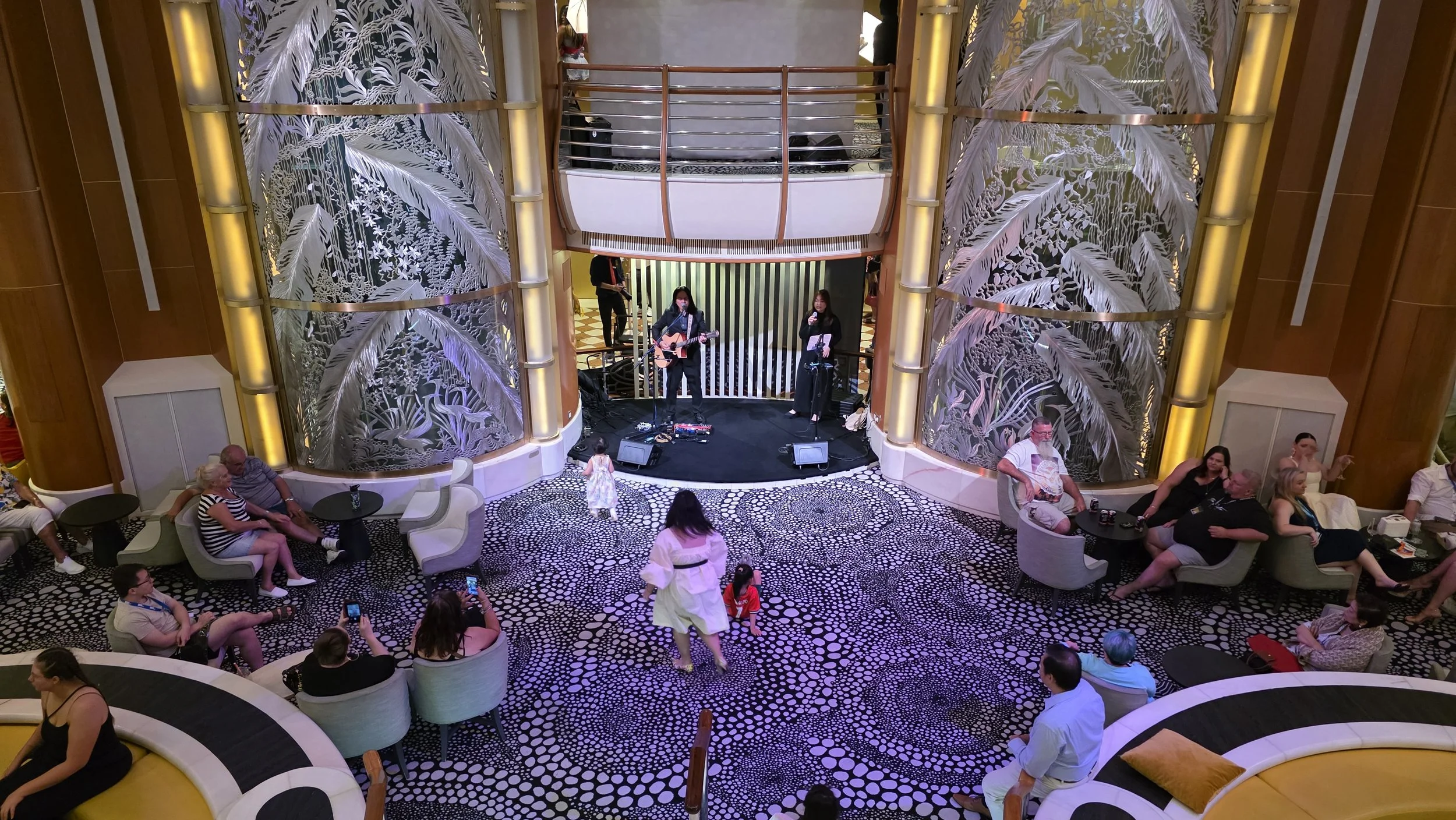 People sitting and watching a live music performance in a lobby with decorative screens and patterned carpet.