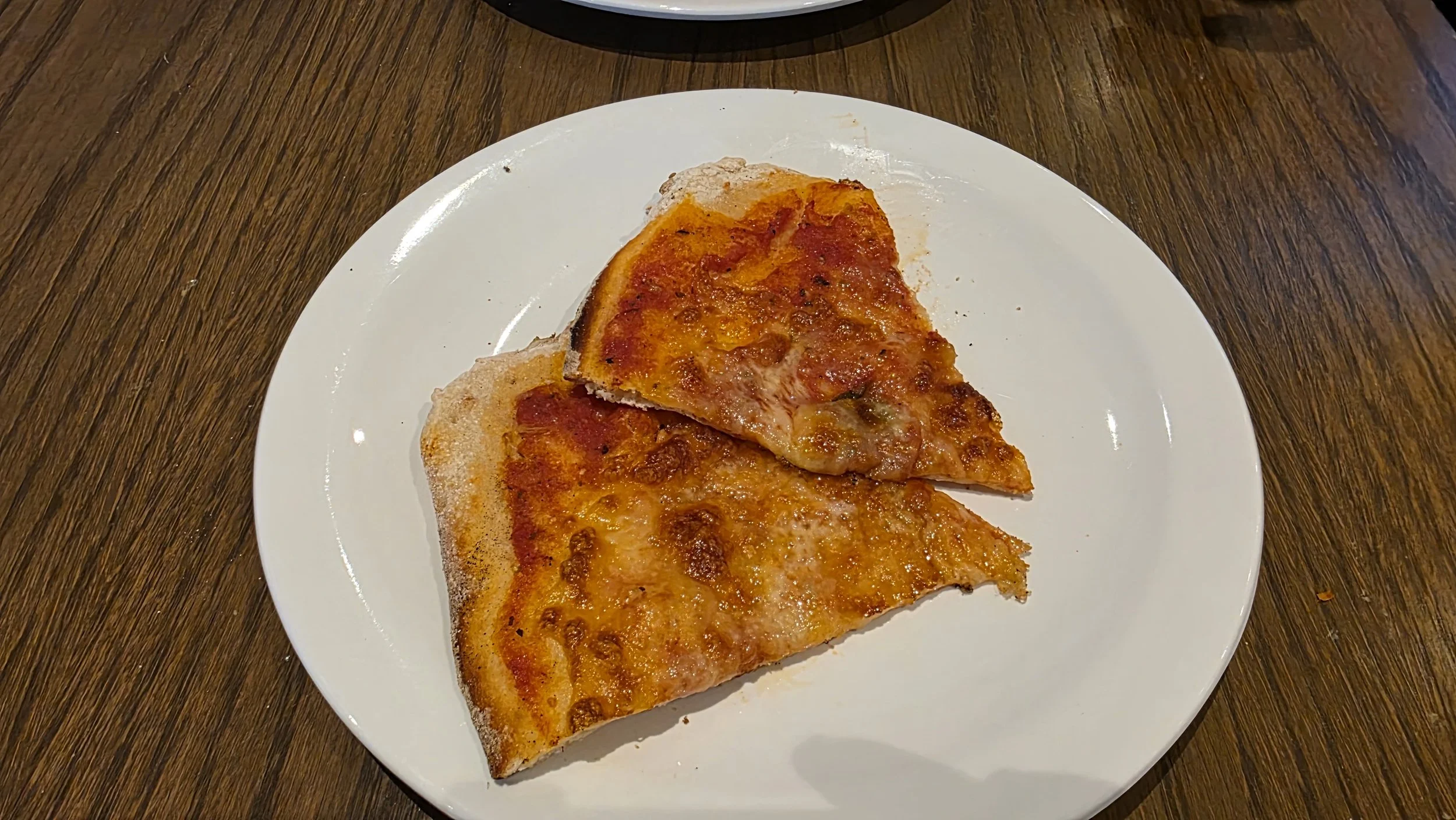 Two slices of cheese pizza on a white plate on a wooden table.