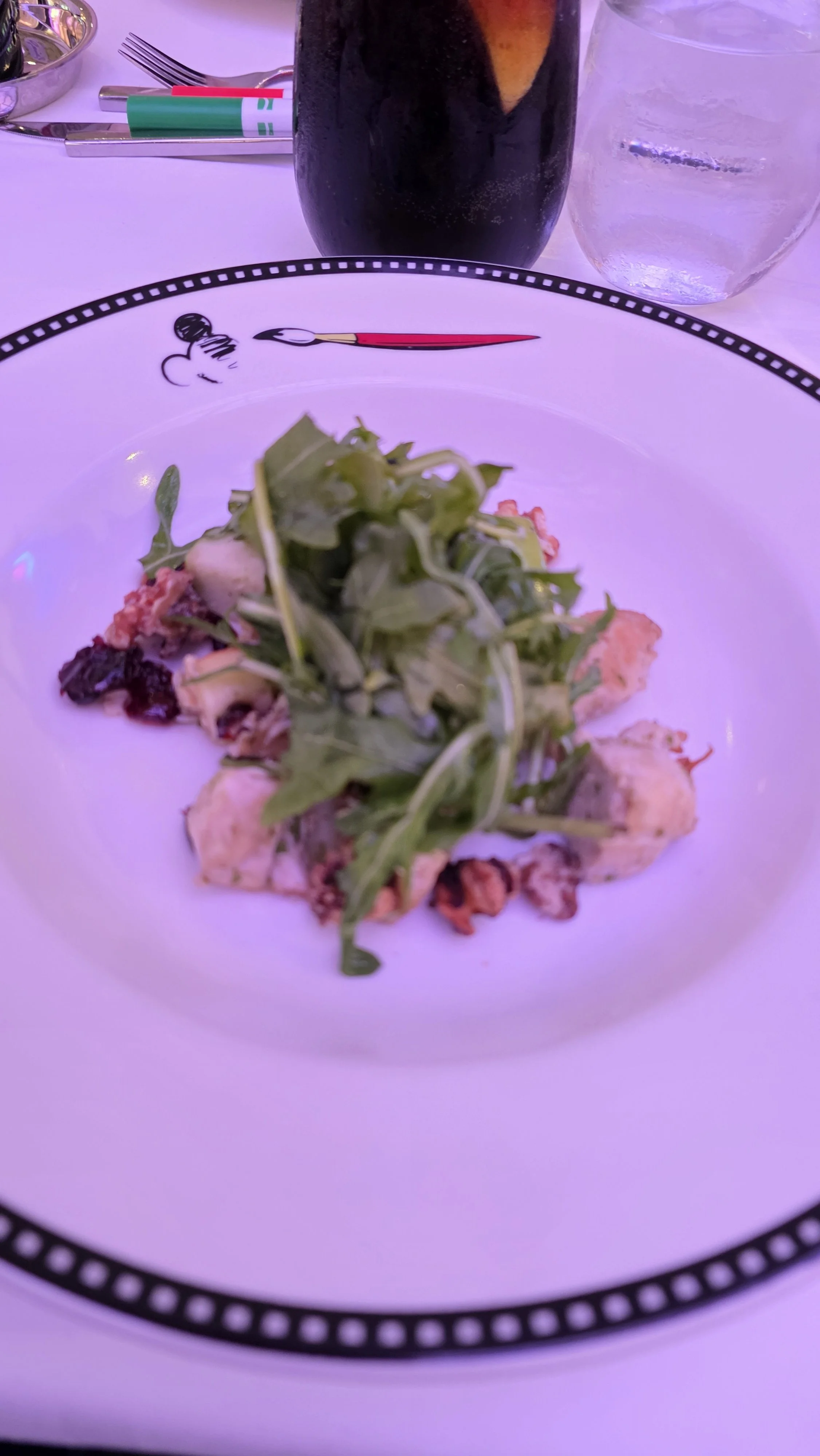 A plate of salad with leafy greens and possibly chicken, with a dark beverage and a glass of water on a table.