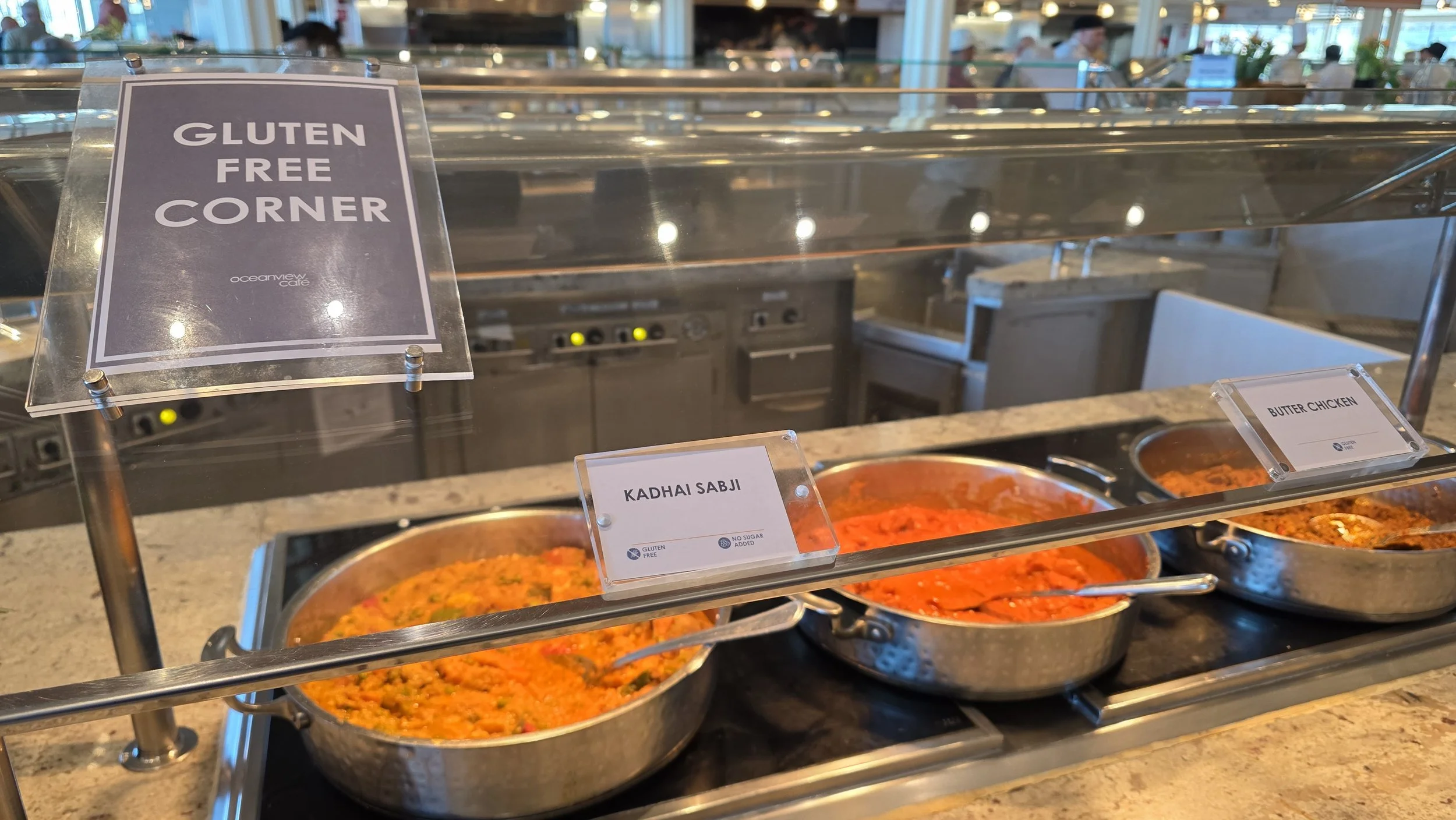 Buffet counter with three pans of Indian dishes labeled Kadhai Sabji, Butter Chicken, and another dish. Sign above states Gluten Free Corner.