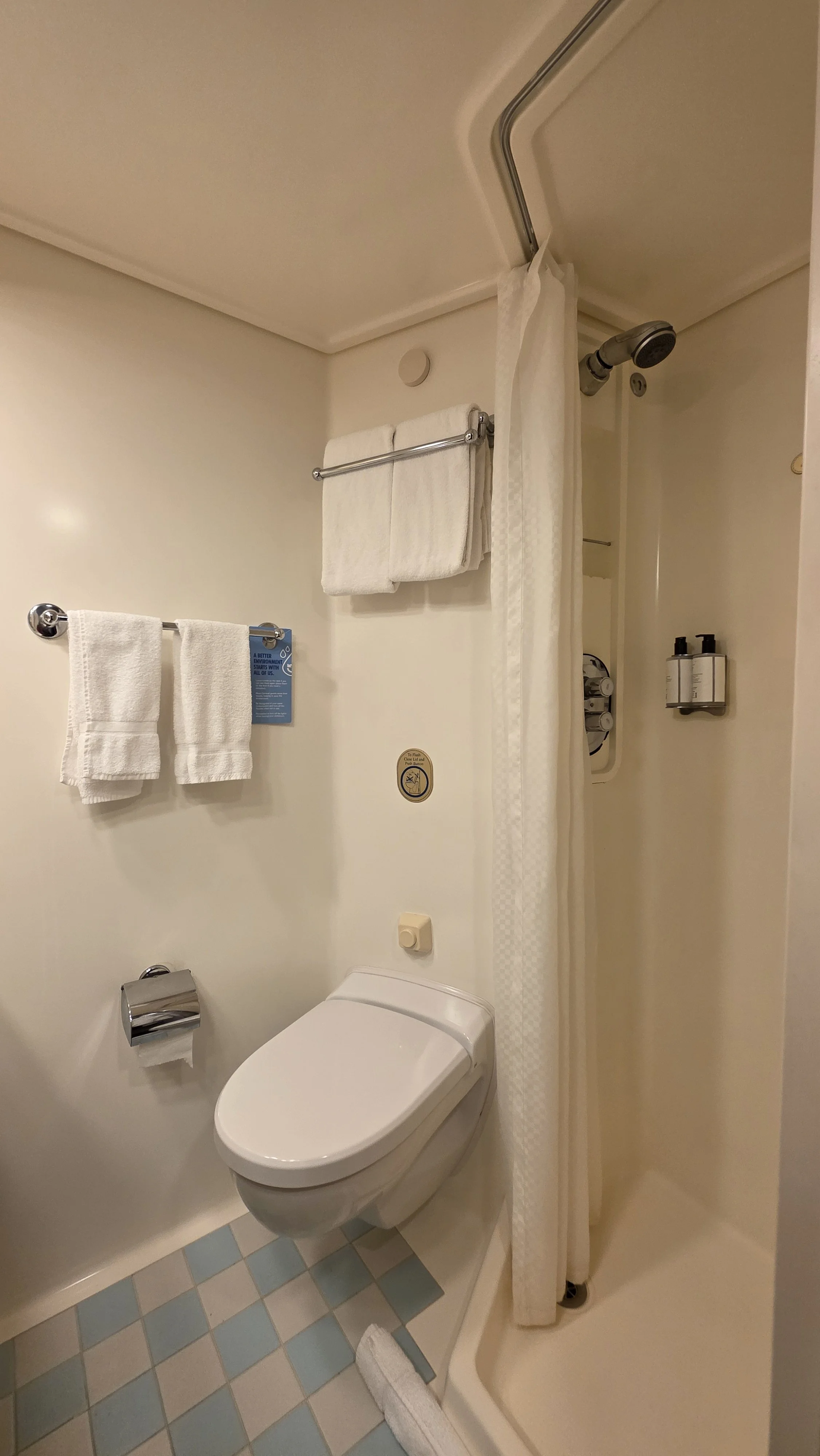A compact hotel bathroom with a toilet, a shower with a curtain, and towel racks with white towels.
