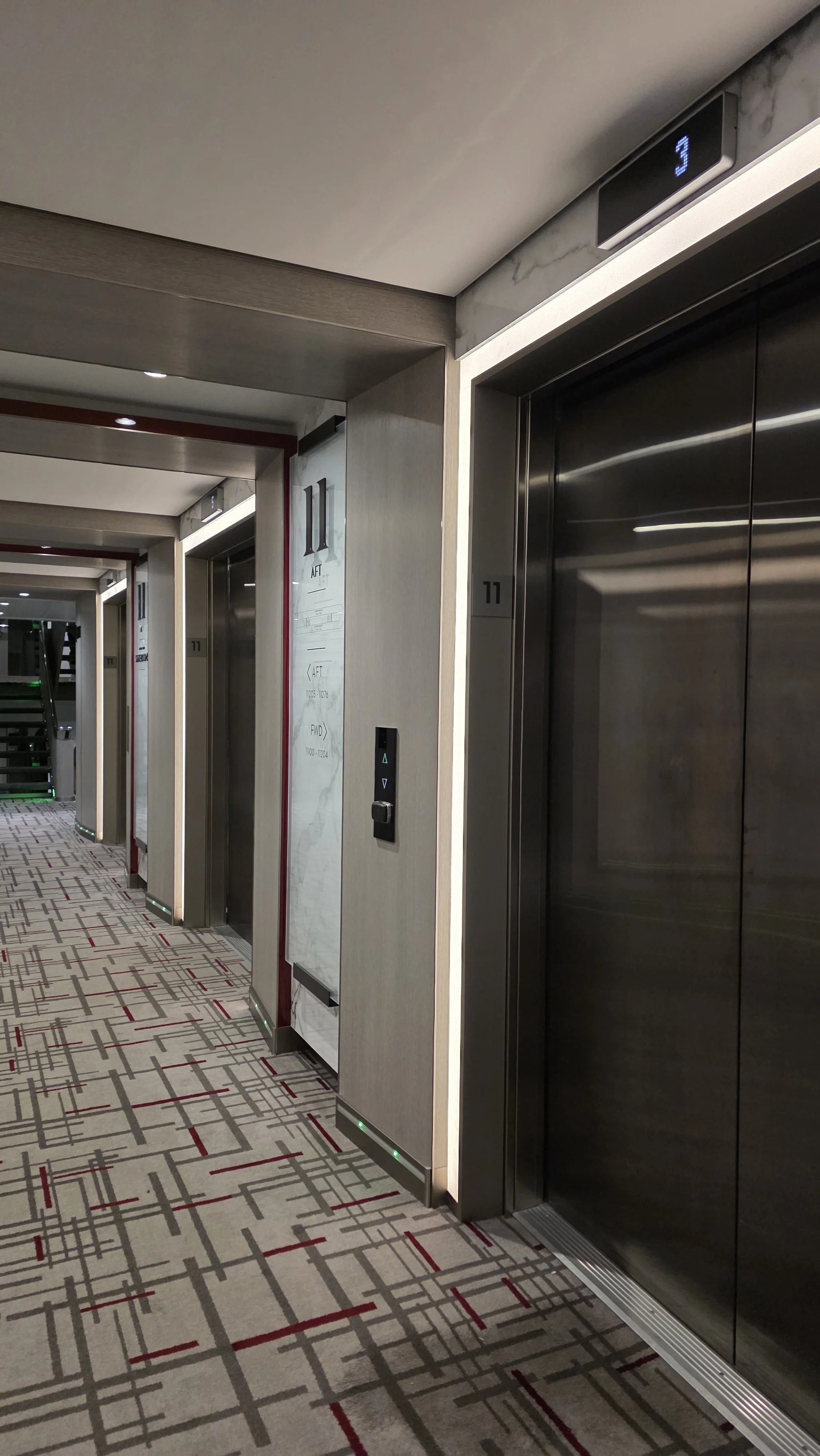 Elevator lobby with three elevators, digital floor indicator showing the number 3, and patterned carpet.