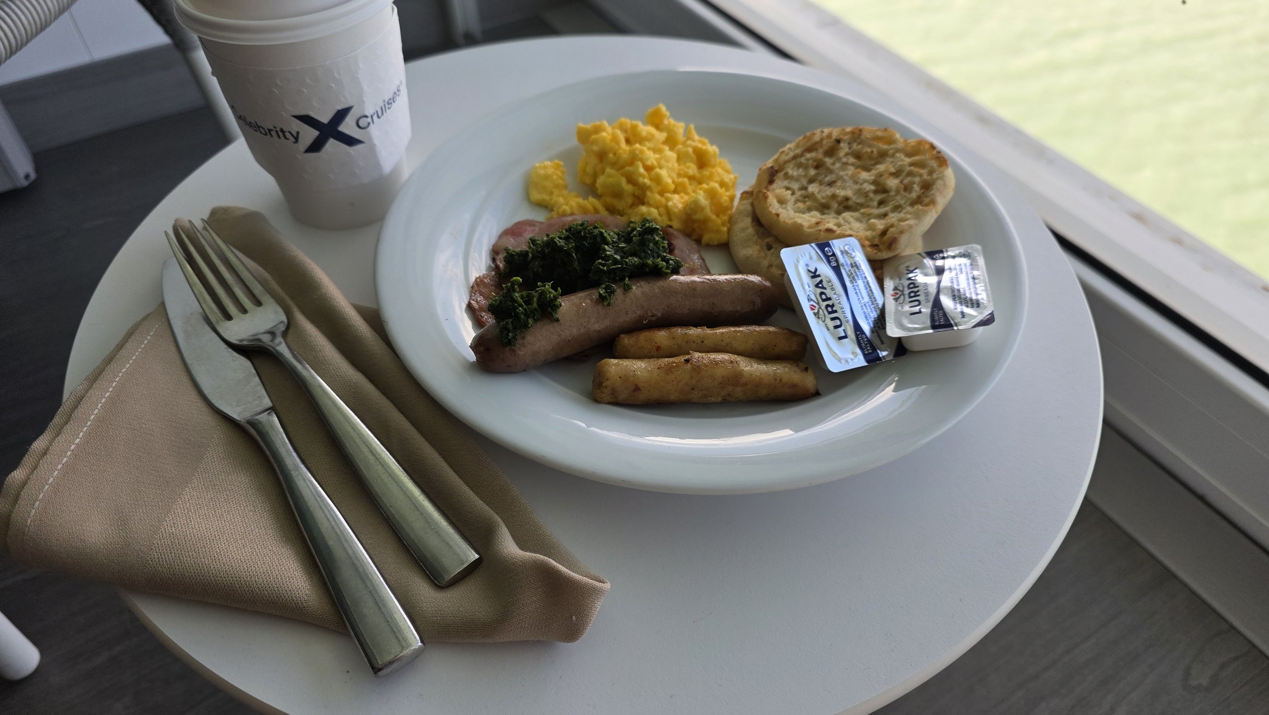 Breakfast plate with scrambled eggs, sausage, hash browns, biscuit, spinach, and sausage gravy on a white plate, with a cup of coffee, napkin, fork, and knife on a beige napkin on a round white table.