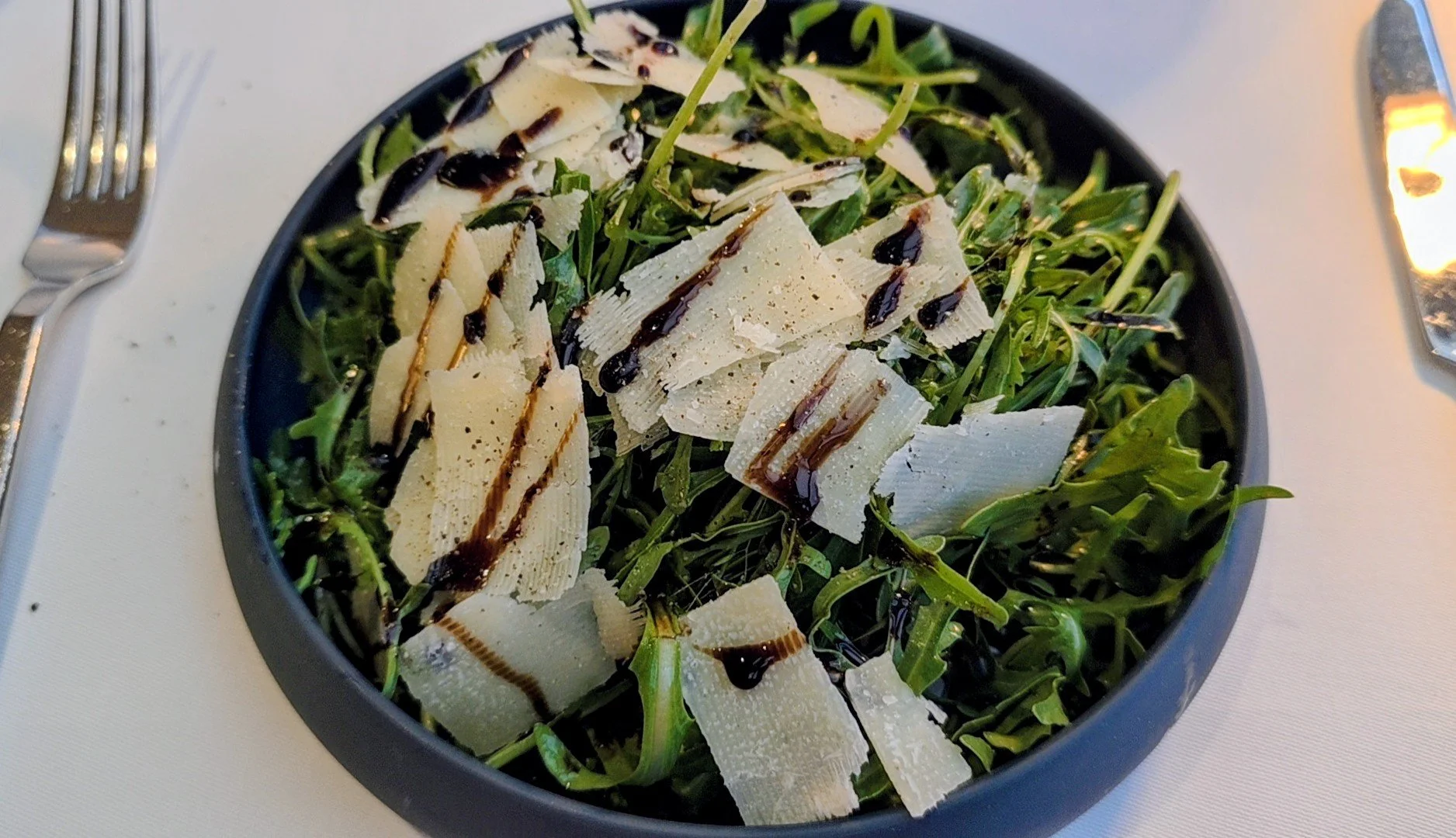 Arugula salad topped with shaved Parmesan cheese and balsamic glaze.