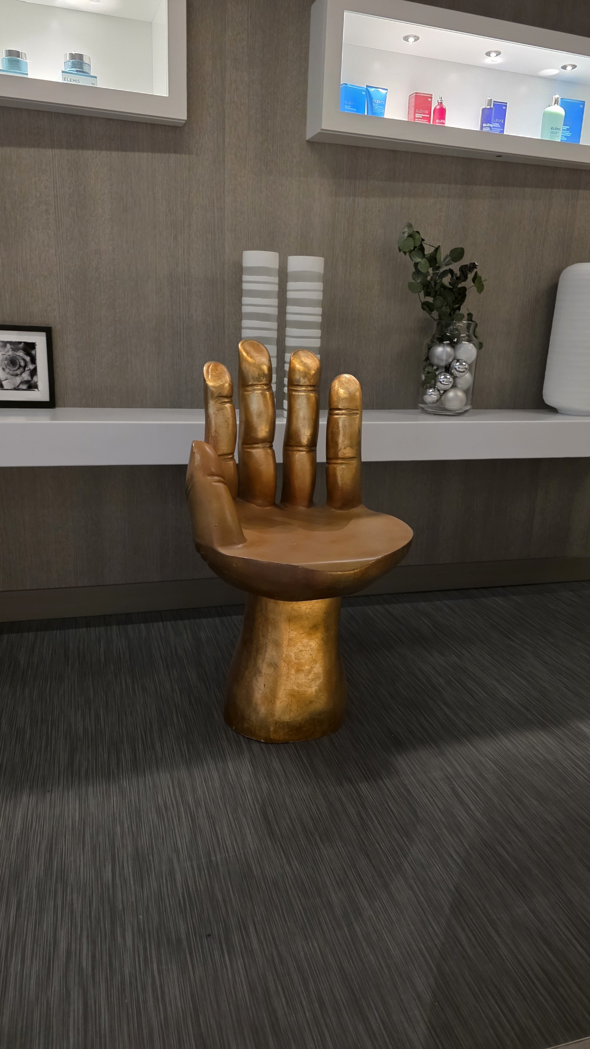 A wooden chair shaped like a human hand, with the fingers as the backrest and the palm as the seat, installed in a modern interior space.