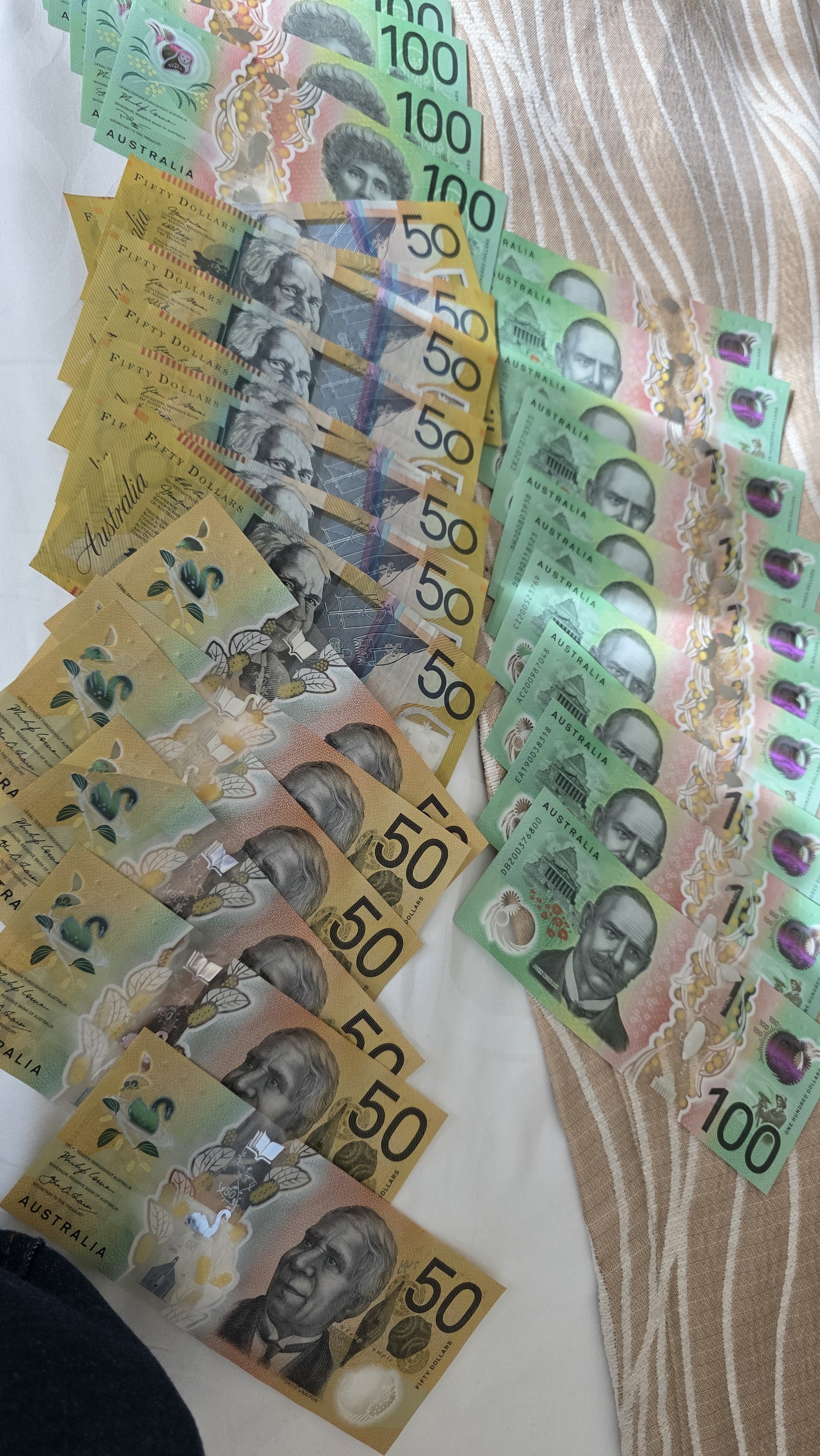 Australian banknotes including fifty dollar bills in yellow, a fifty dollar bill in brown, and a hundred dollar bill in green, laid out on a surface with a cloth underneath.