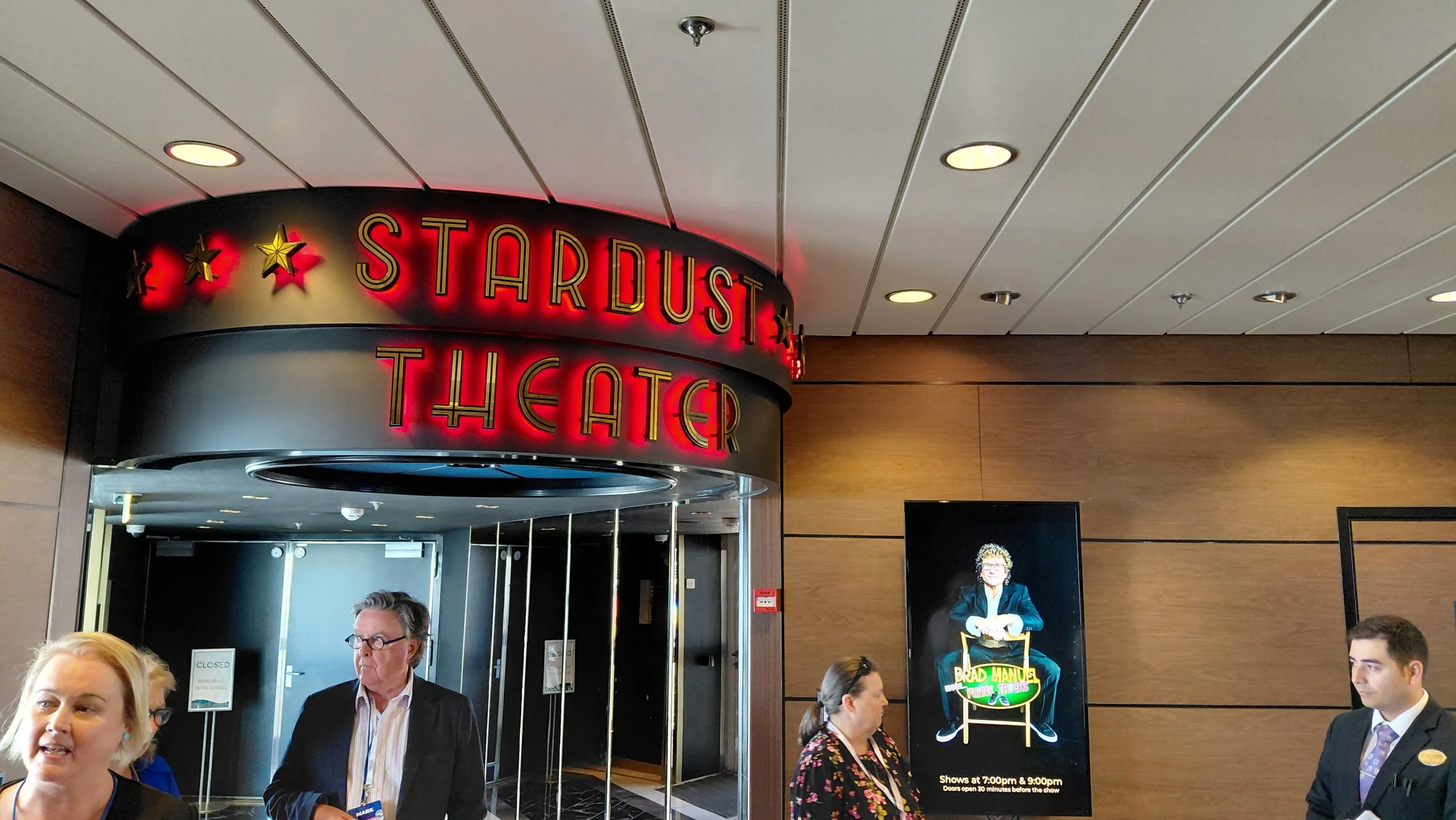 People gathered outside the entrance of Stardust Theater, with a neon sign overhead and a digital poster advertising a show.
