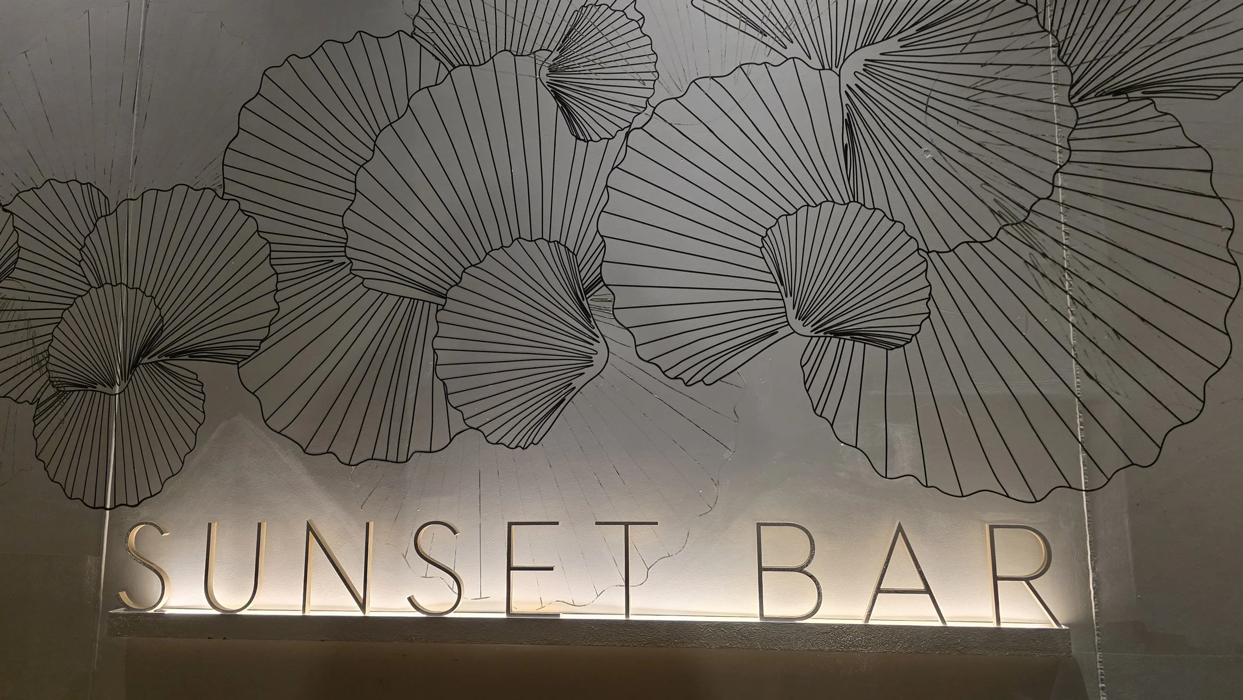 Decorative wall with black line drawings of ginkgo leaves and illuminated text reading 'Sunset Bar'.