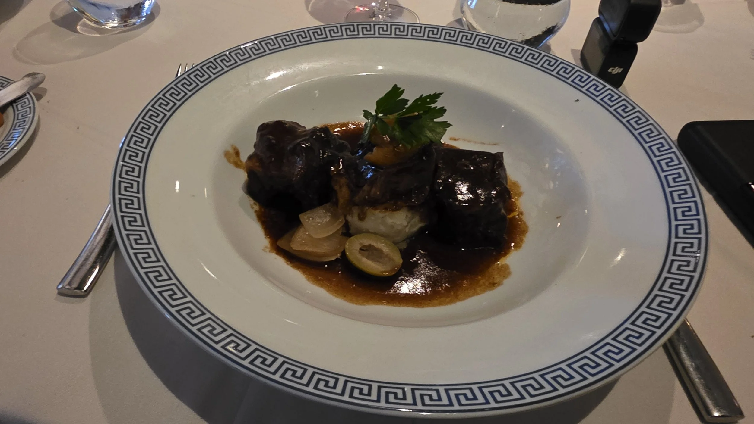 Plate of braised beef stew with chunks of beef in a dark sauce, served with sliced onions and garnished with a sprig of parsley.