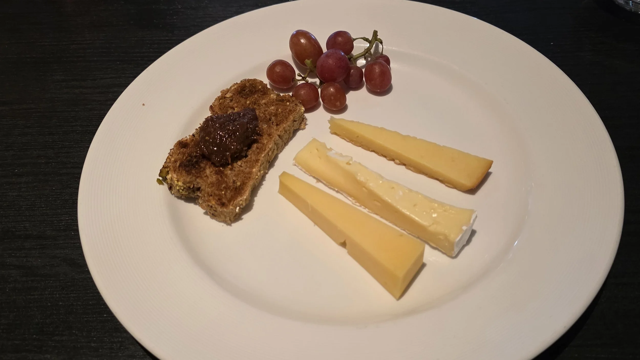 Plate with grapes, three types of cheese, and a slice of loaf with jam.