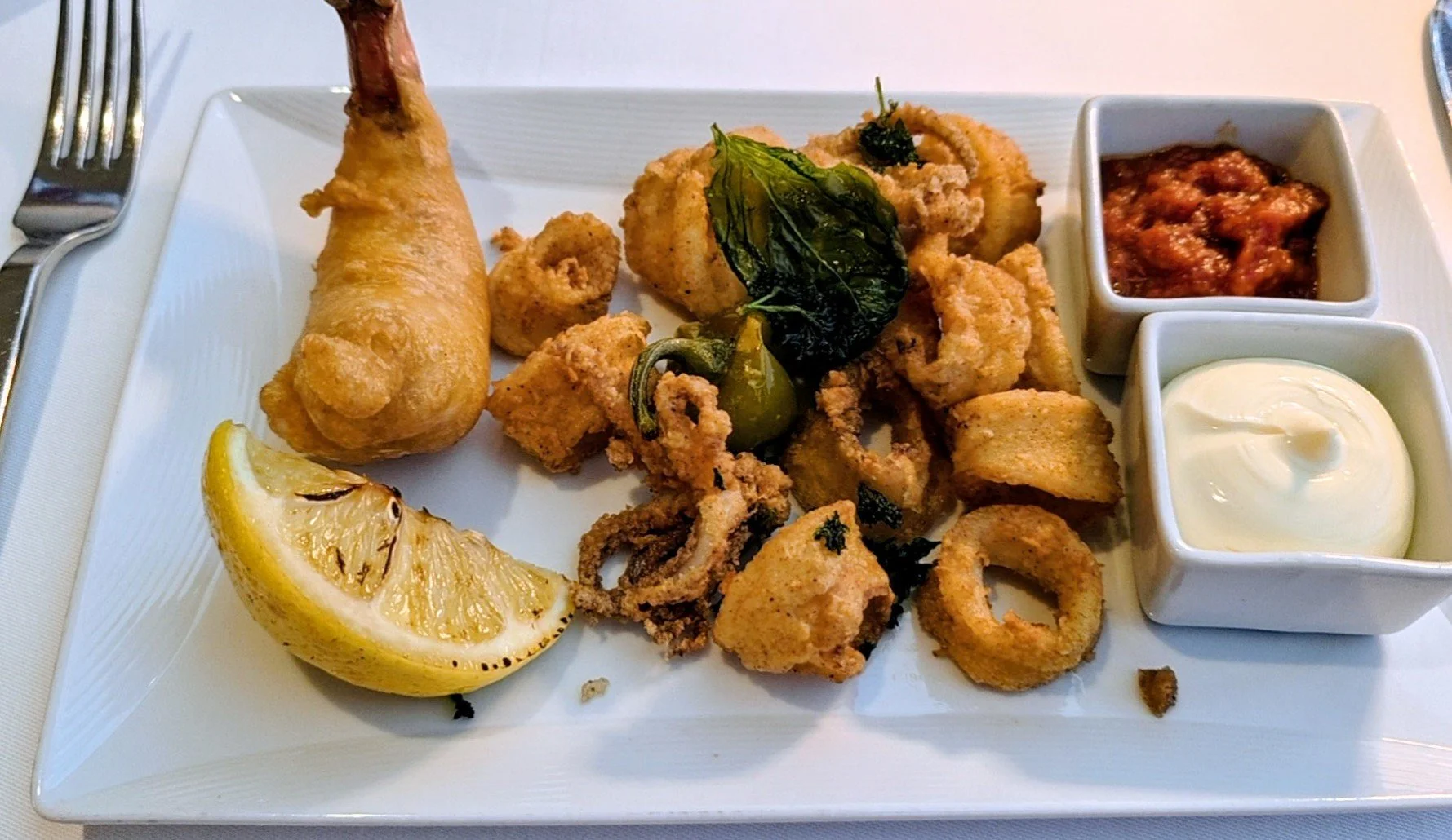 A plate of fried seafood with lemon wedge and two small bowls of dipping sauces.
