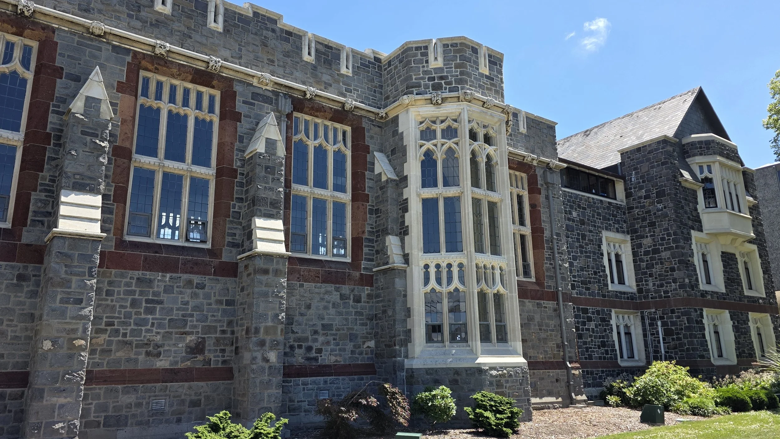 Close-up view of a historic stone building with gothic-style windows, decorative stonework, and a turret under a clear blue sky.