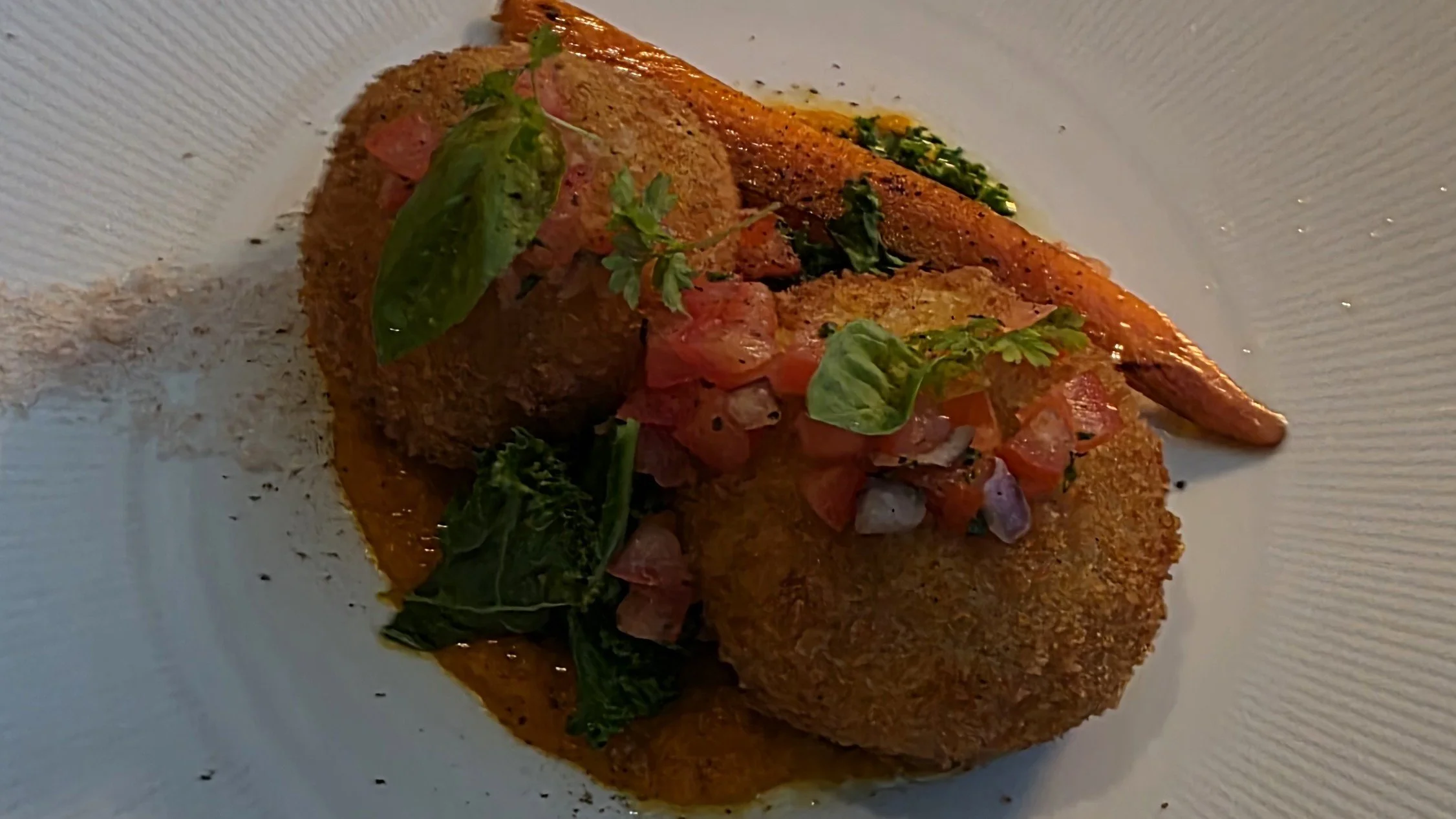 Fried croquettes topped with salsa and herbs, served with a side of vegetables and sauce, on a white plate