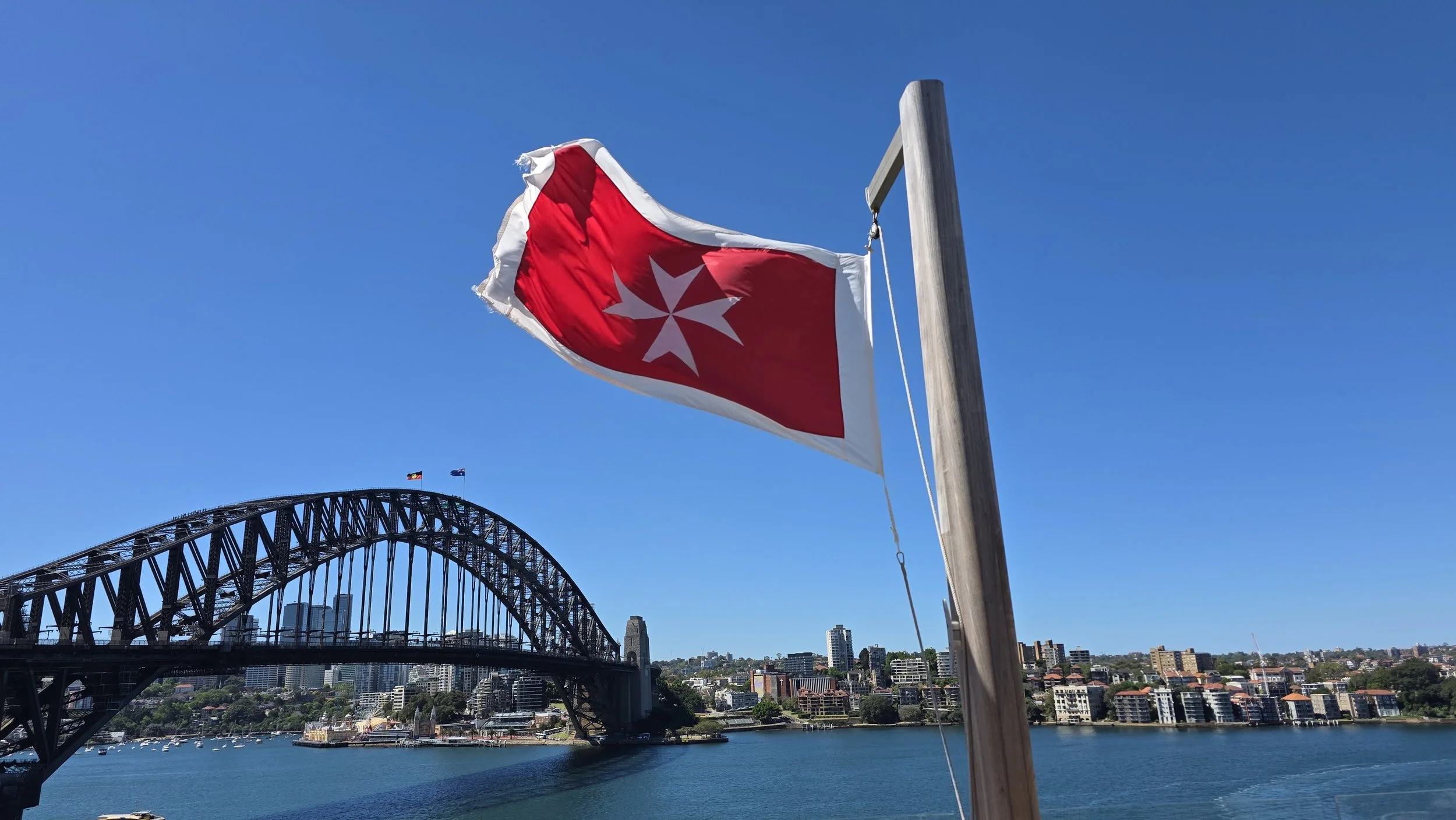 The Sydney Harbour Bridge in Australia with a red and white maritime signal flag blowing in the wind against a clear blue sky.