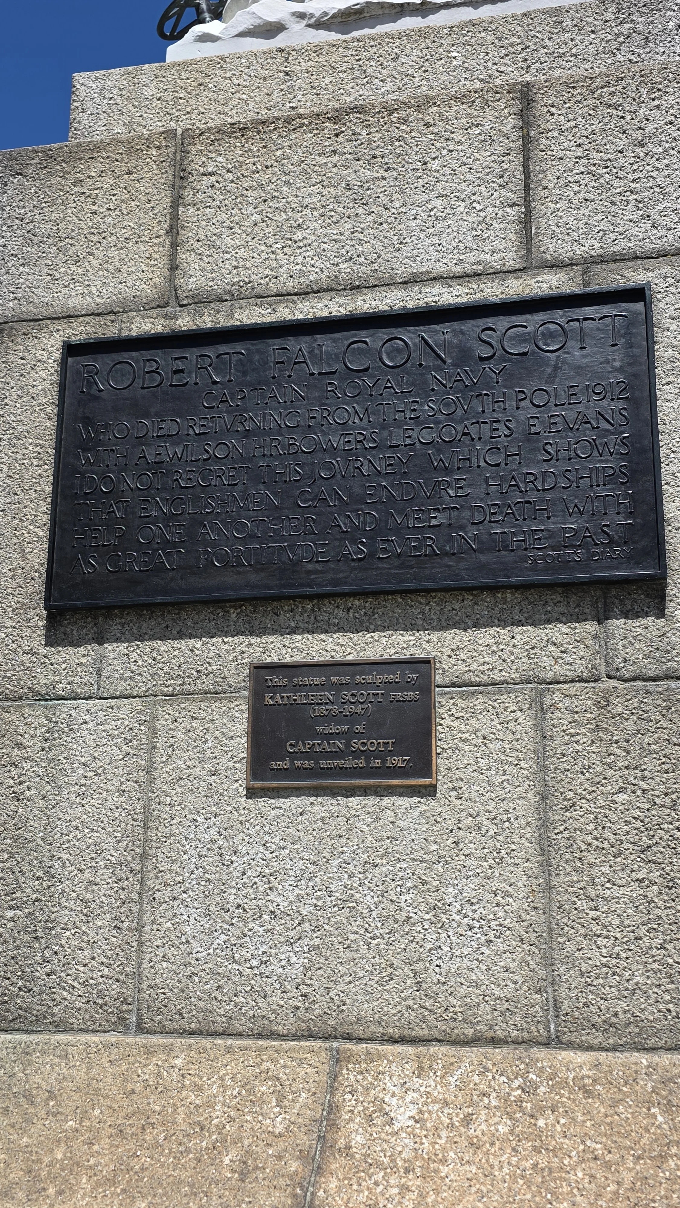 A memorial plaque mounted on a stone wall honoring Captain Robert Falcon Scott, who died returning from the South Pole in 1912, with an inscription about his journey, along with a smaller plaque noting the sculpture was created by Kathleen Scott, wid