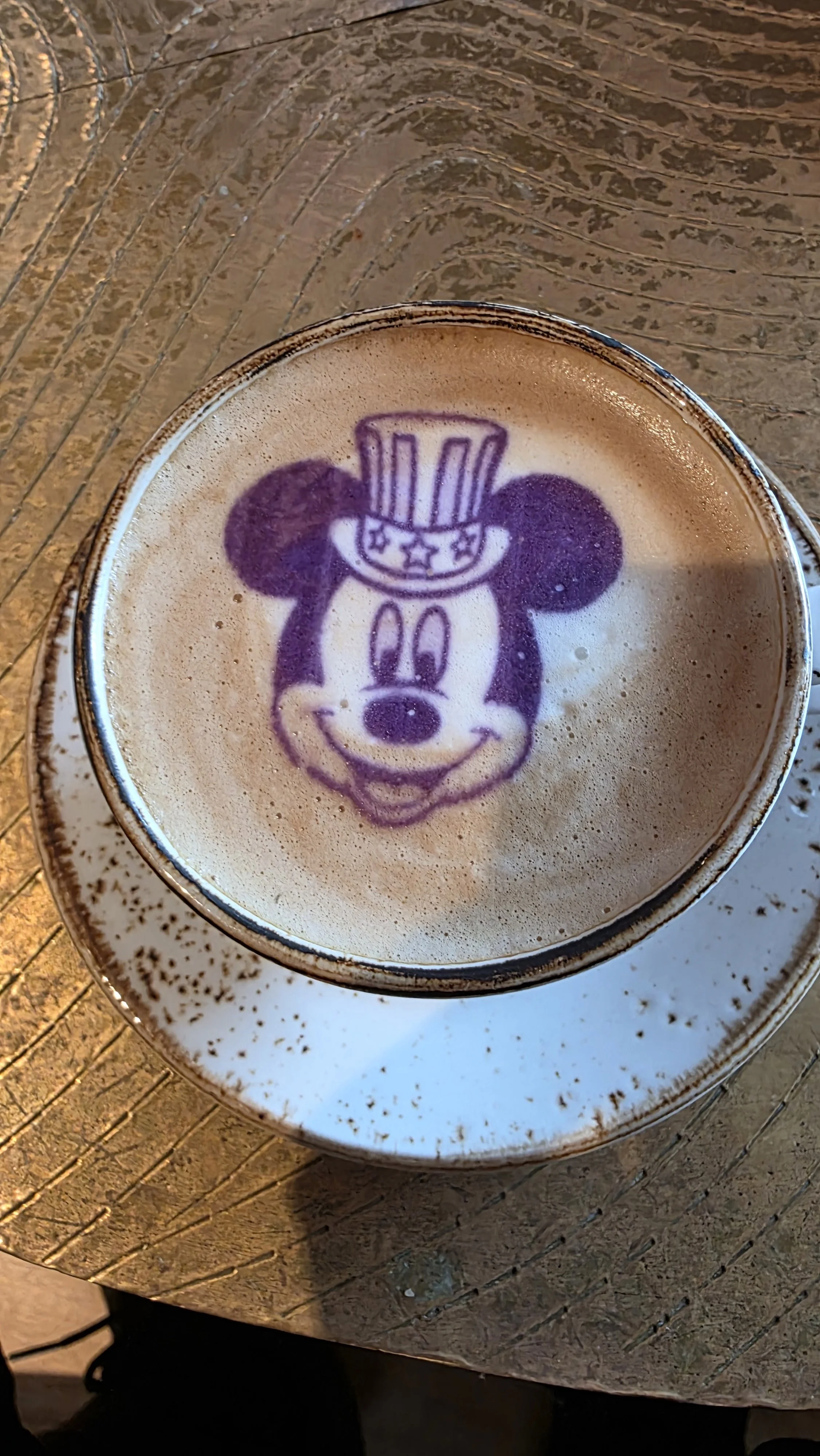 A cup of coffee with a latte art of Mickey Mouse wearing a Uncle Sam hat.