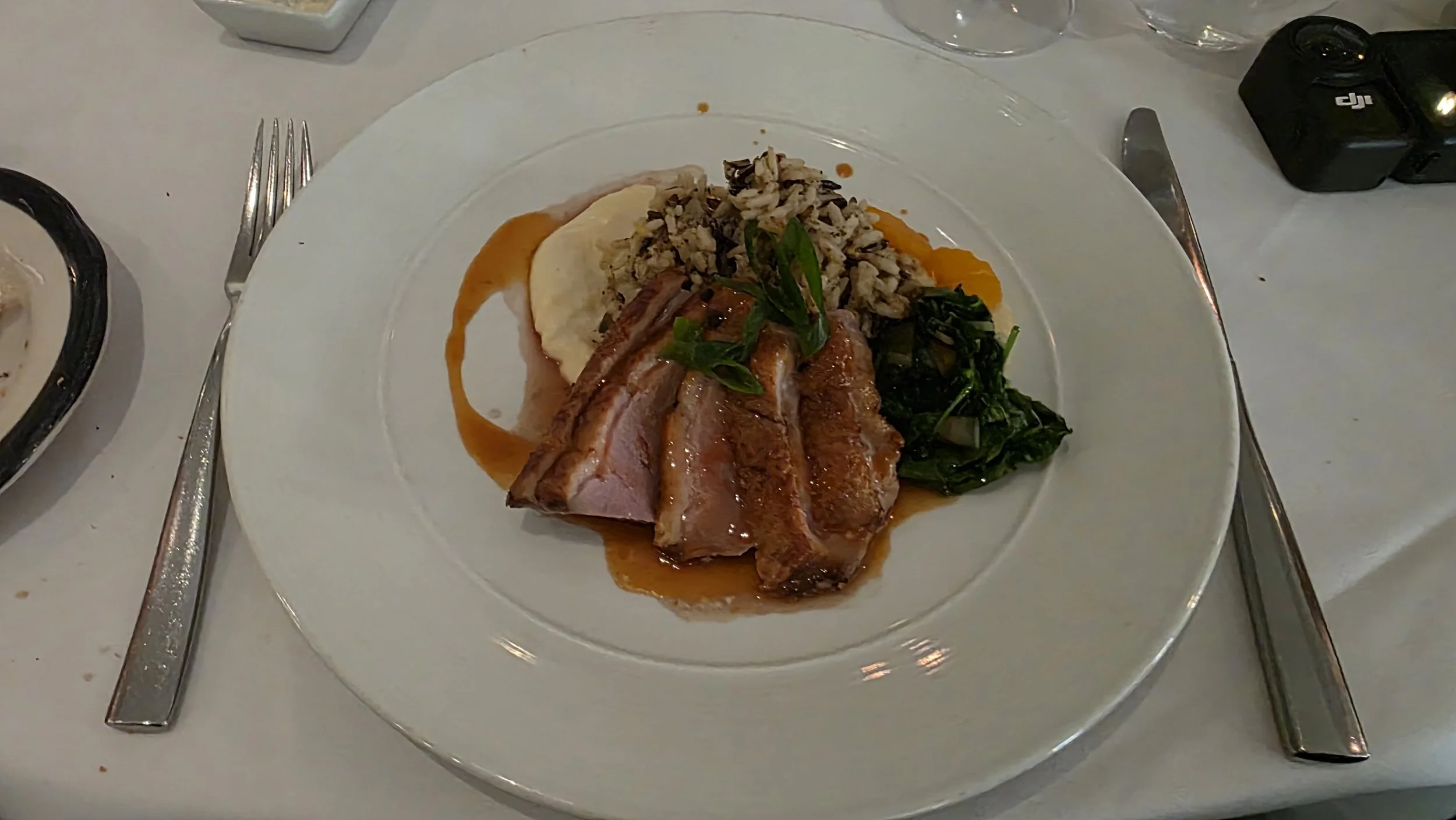 A plated meal featuring slices of glazed ham, mashed potatoes with gravy, sautéed greens, and a serving of rice with vegetables, garnished with fresh herbs, on a white dinner plate.