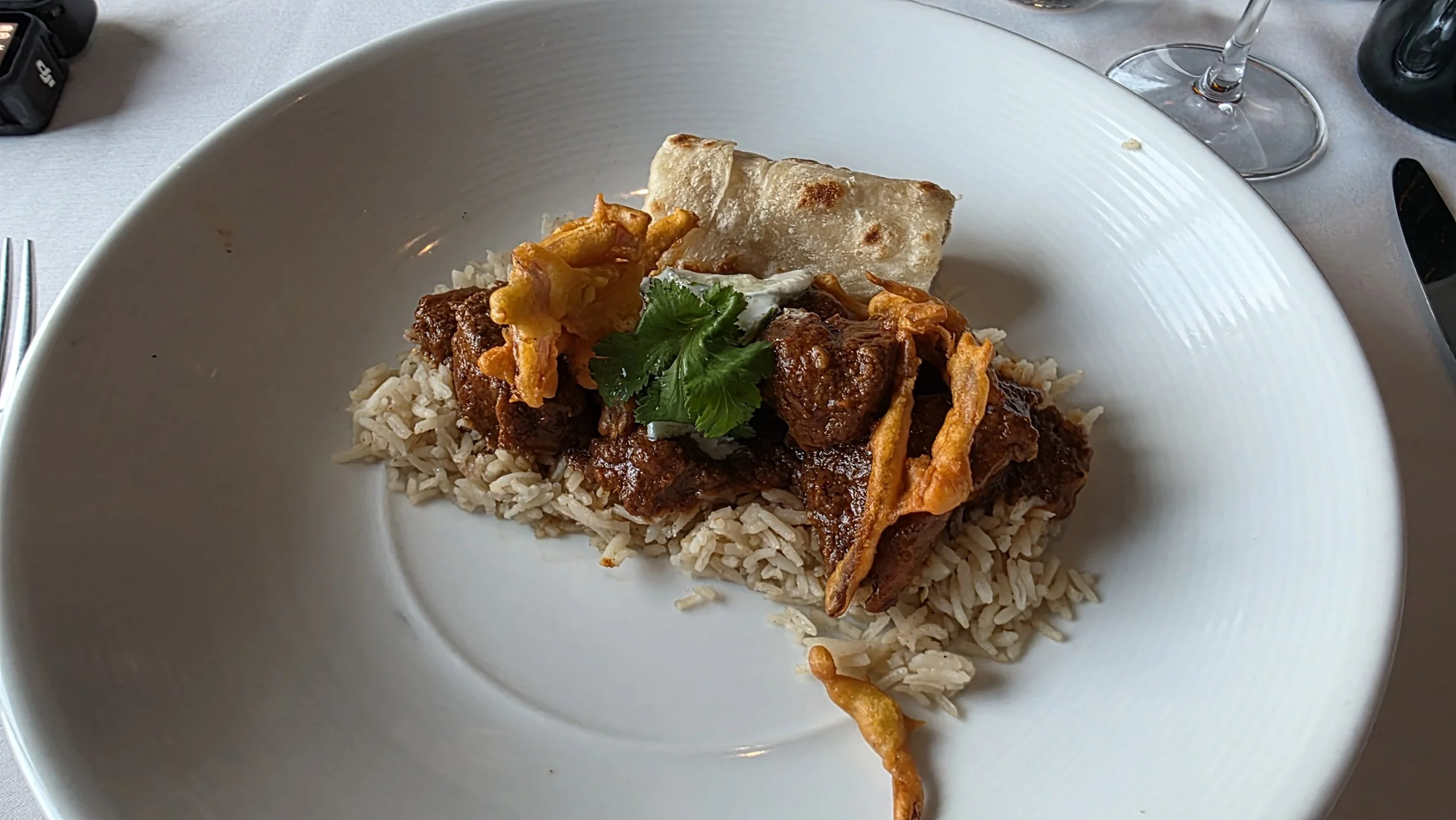 Plate of rice topped with beef stew, fried vegetables, a piece of flatbread, and garnished with cilantro.