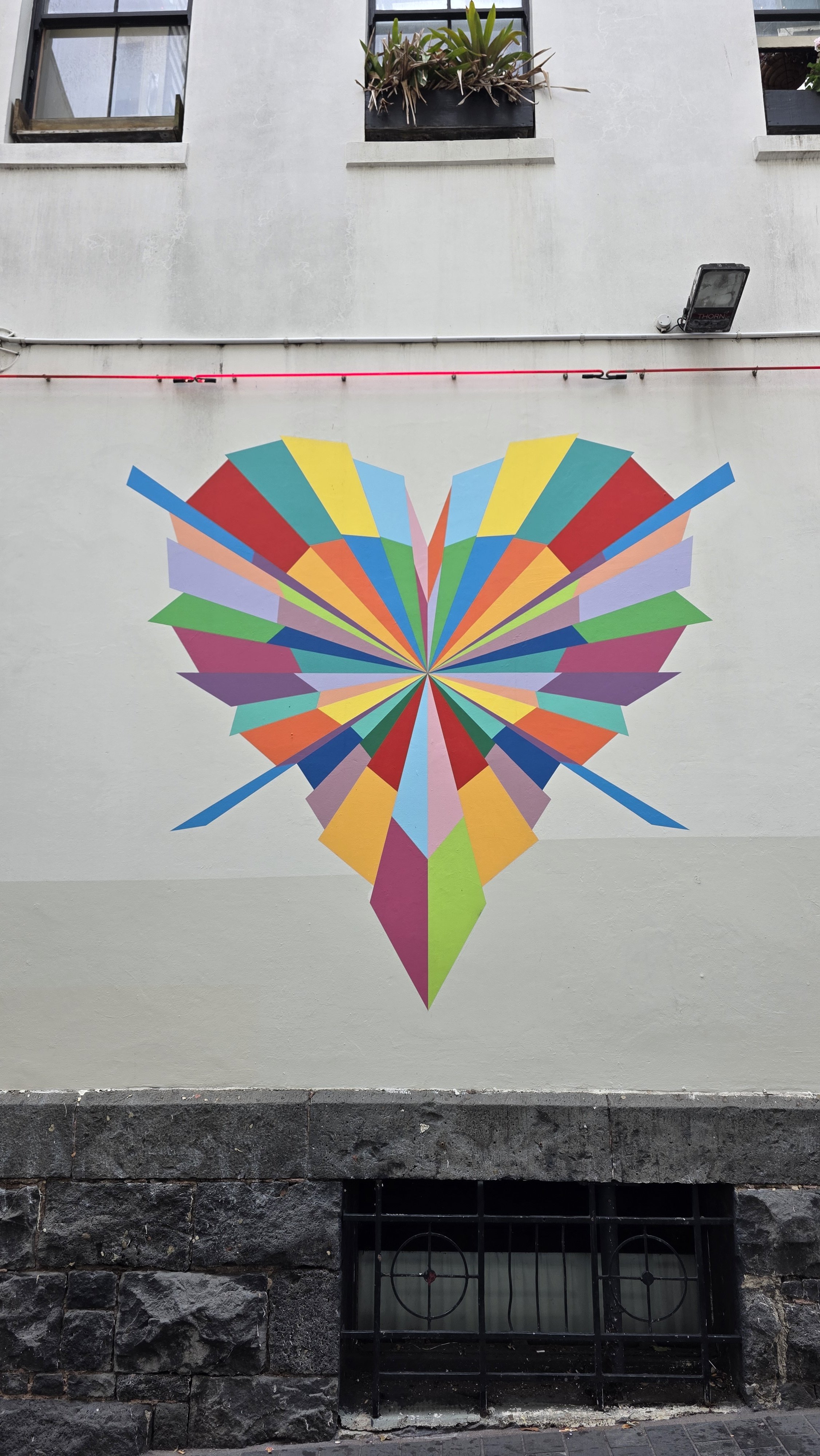 Colorful heart-shaped mural composed of geometric shapes on a building wall and a small window below.