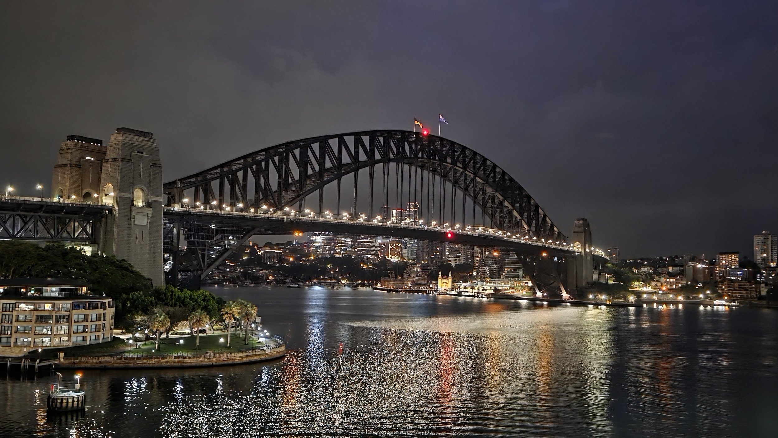 Nighttime view of Sydney Harbour Bridge with city lights reflecting on the water.