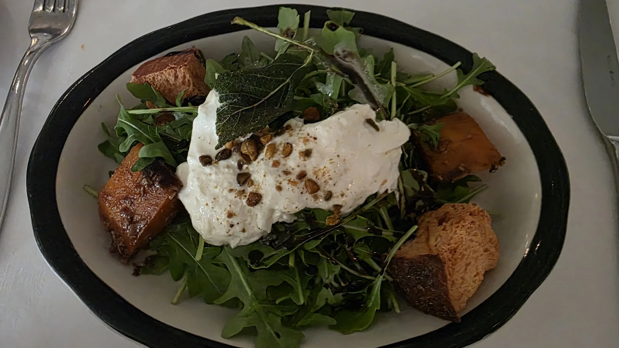 Salad with roasted sweet potatoes, arugula, and burrata cheese topped with black pepper and nuts.
