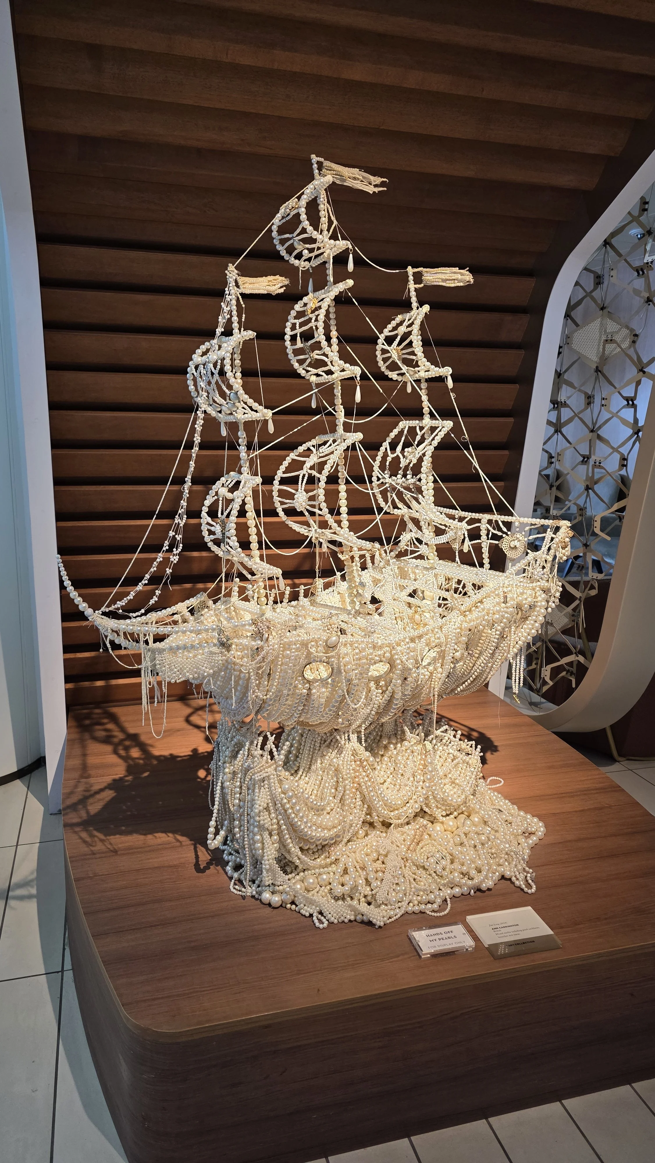 A ship sculpture made entirely of pearls, crafted to resemble a sailing vessel, displayed on a wooden surface.