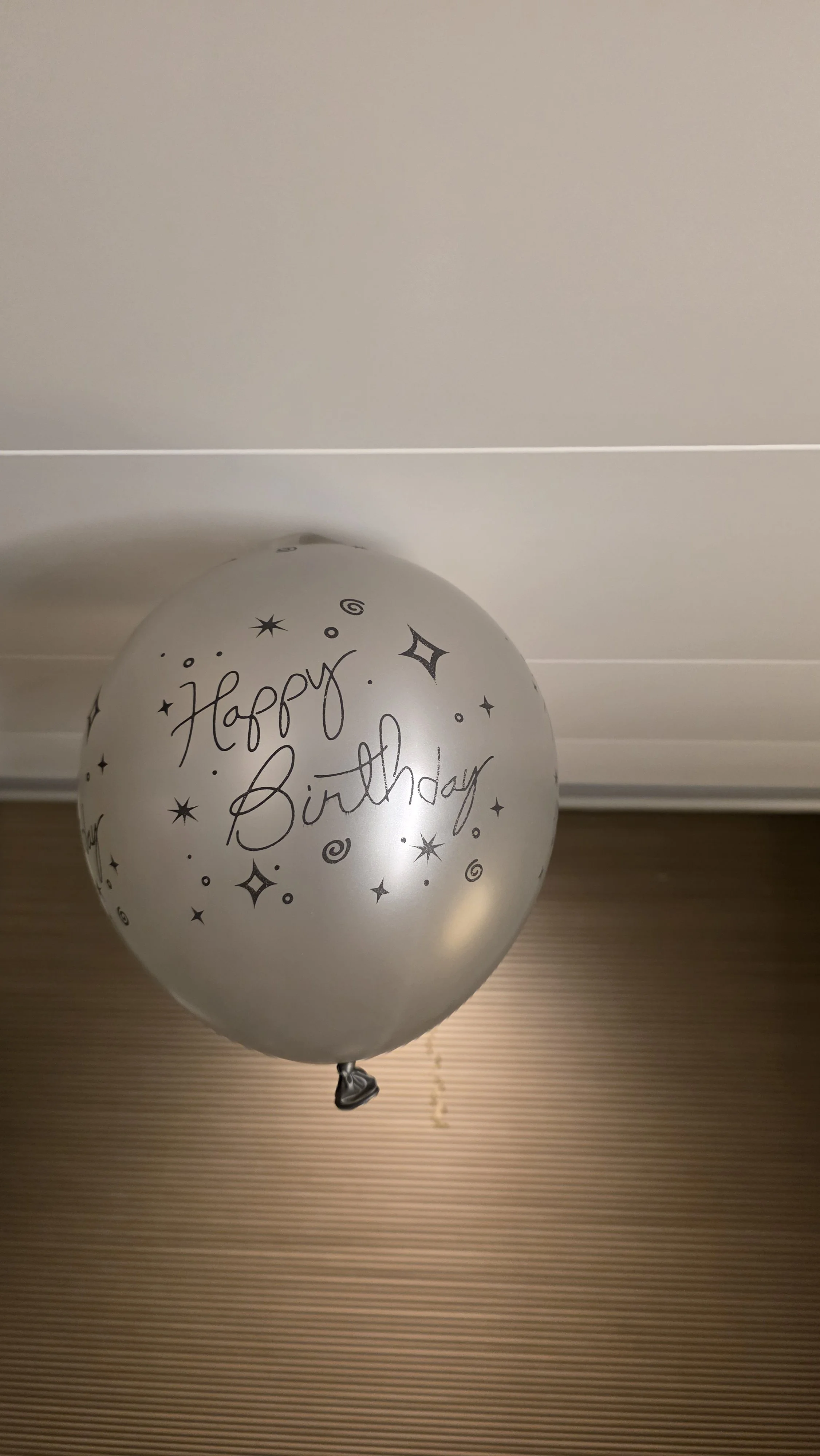 Silver birthday balloon with black 'Happy Birthday' text and star and swirl designs, hanging from the ceiling.