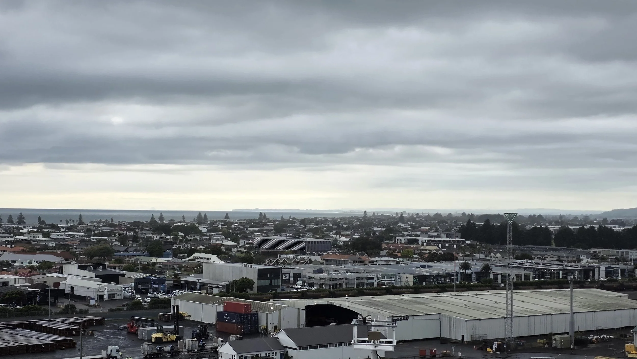 Overcast sky with gray clouds over a cityscape with industrial buildings, warehouses, and residential areas in the distance.
