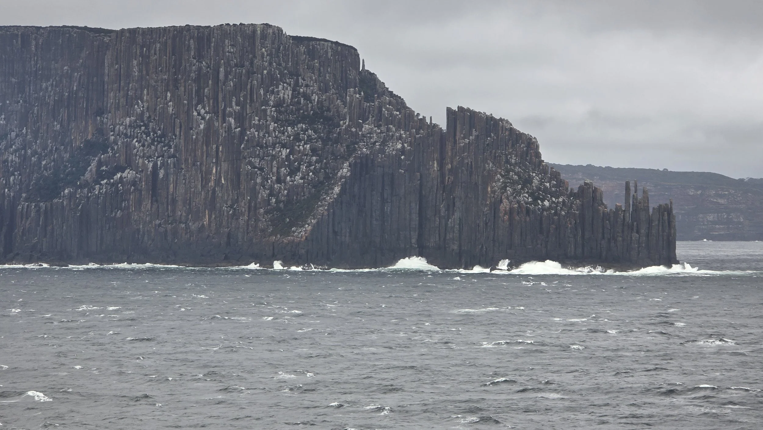Cliffside rock formations along the ocean under cloudy sky.