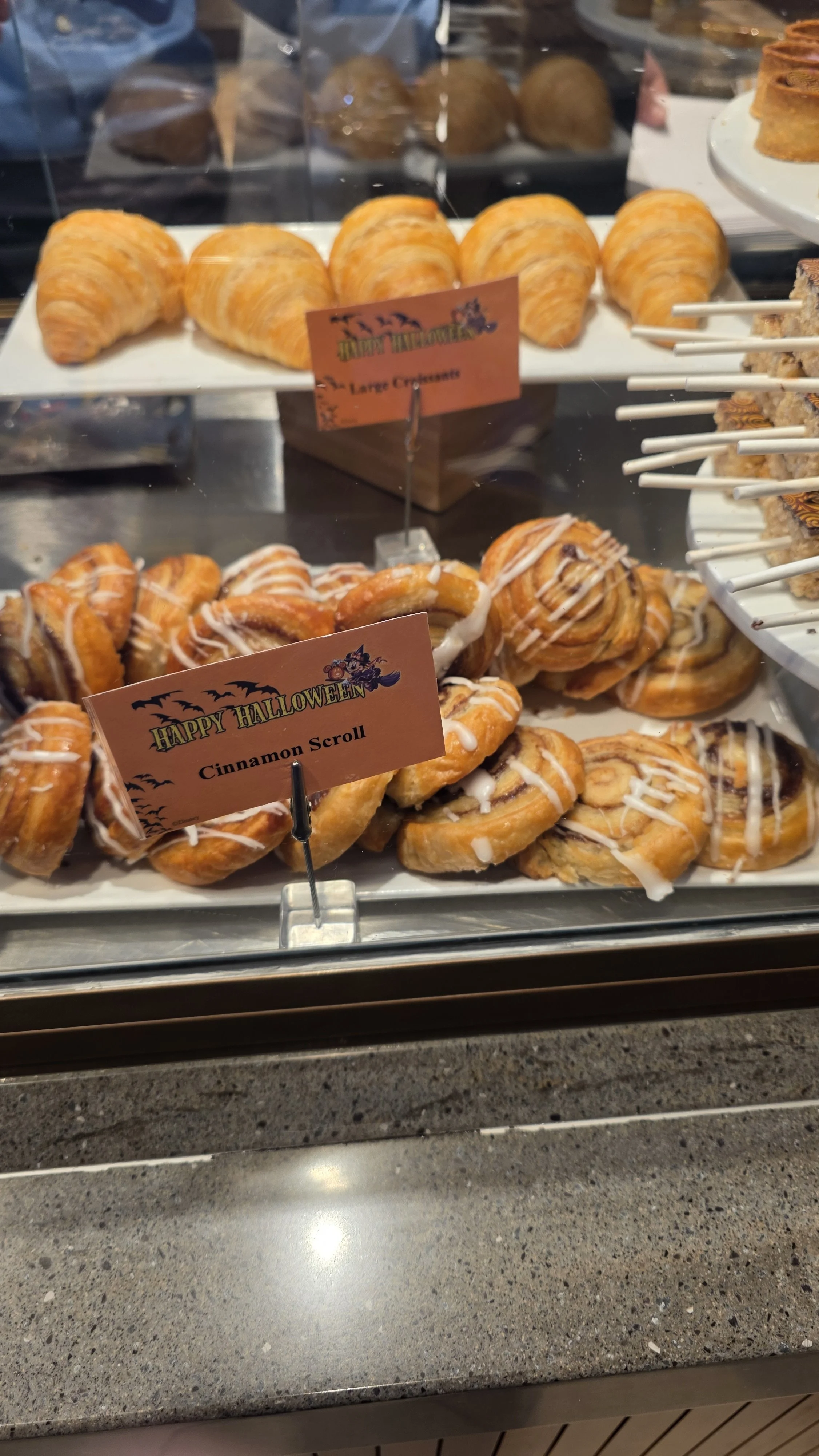Display case with Halloween-themed cinnamon scrolls decorated with white icing and a sign that reads "Cinnamon Scroll."