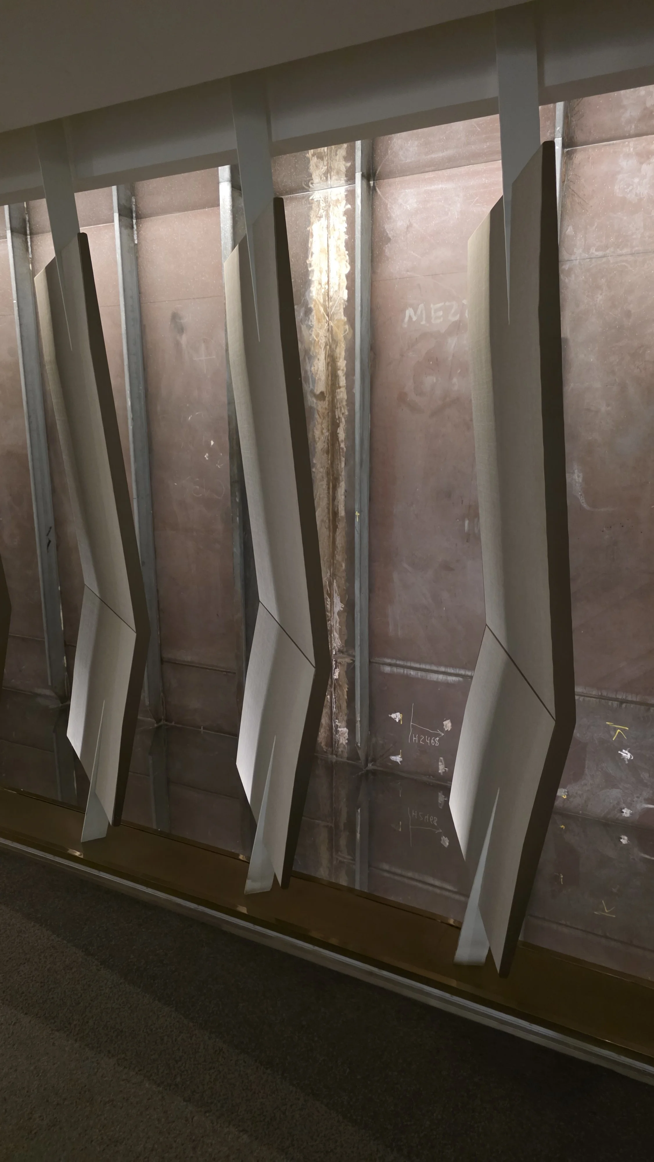 Interior view of a building under construction showing vertical metal studs, insulation, and drywall panels leaning against the wall.