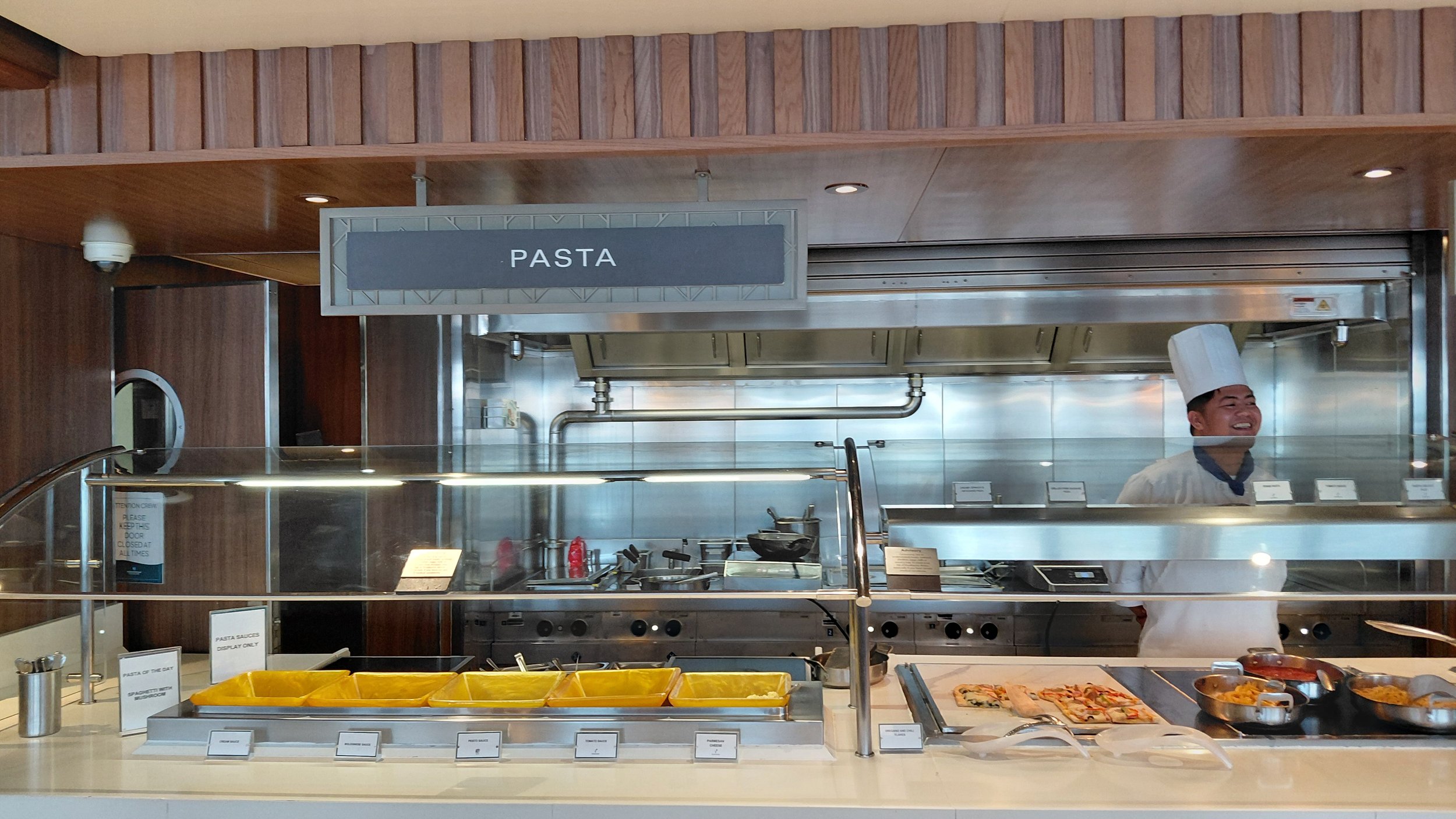 Chef standing behind a pasta buffet station at a restaurant, with various pasta dishes and ingredients on display.