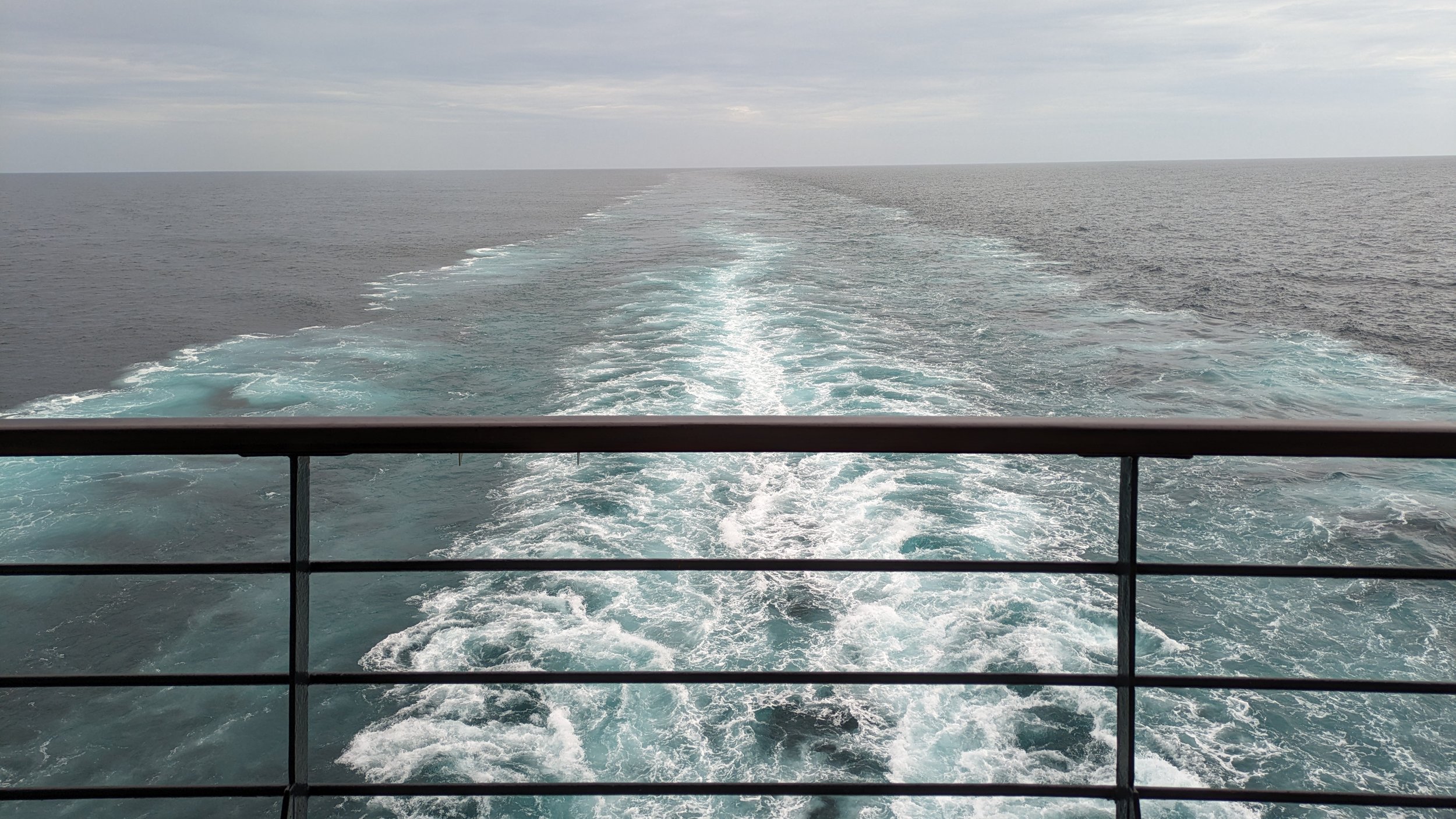 View from the back of a boat showing the wake in the water and the open ocean with overcast sky