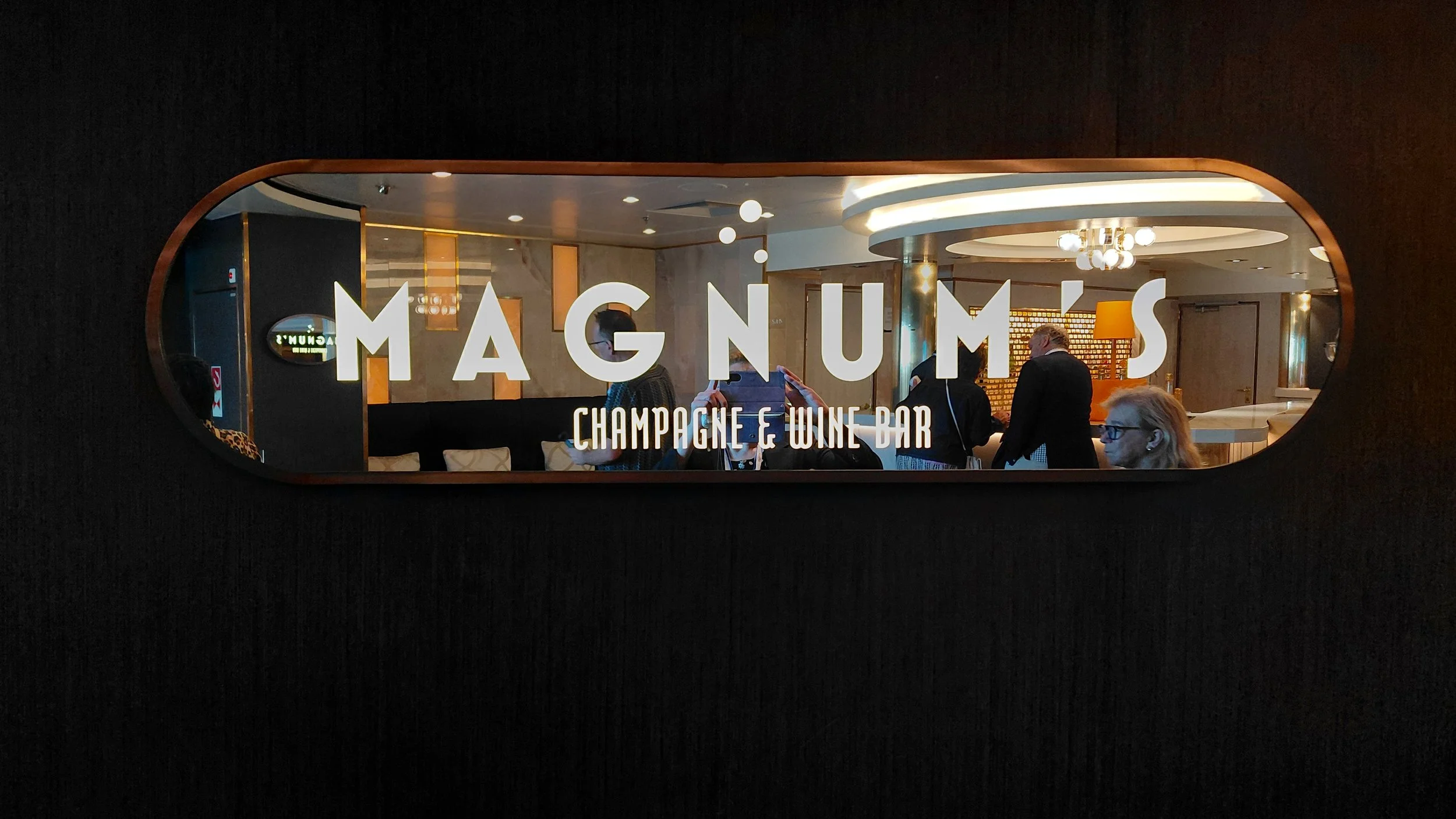 Reflective sign reading 'Magnus Champagne & Wine Bar' with interior of people socializing and bar in the background.