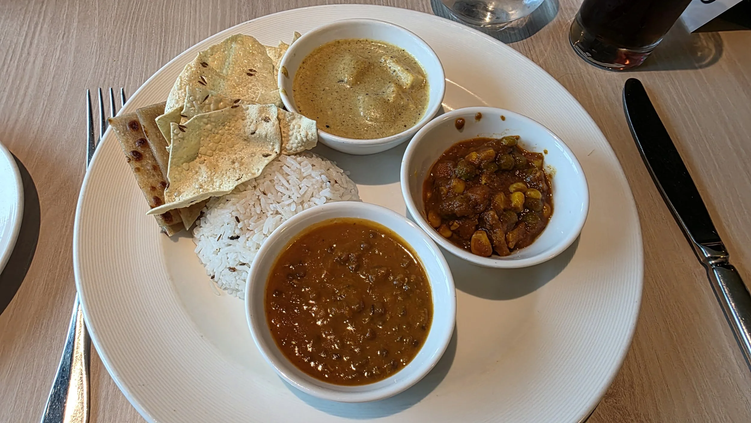 Plate with rice, assorted Indian bread, and three small bowls of curry, one with a yellowish sauce, one with a brown spicy sauce, and one with a green vegetable curry.