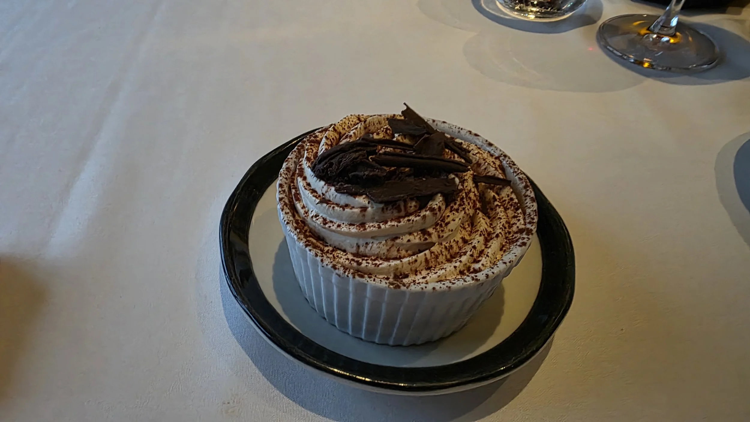 Chocolate and vanilla ice cream sundae topped with chocolate shavings on a white table with wine glasses in the background.