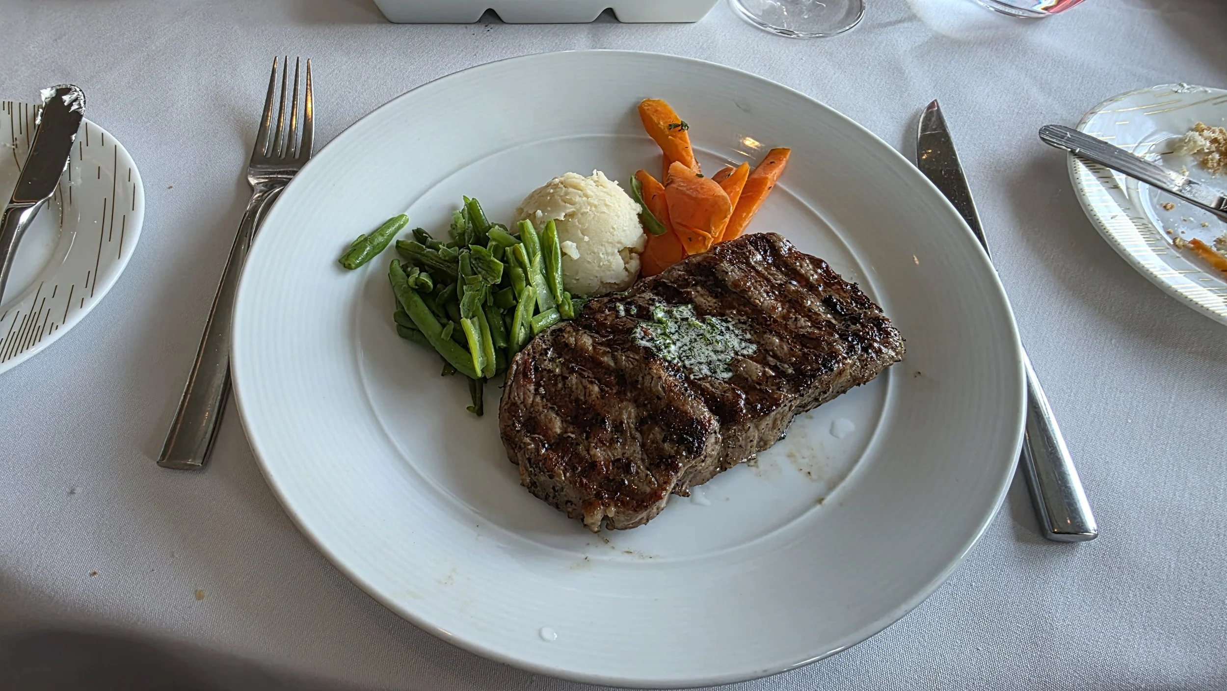 Steak with green beans, mashed potatoes, and carrots on a white plate.
