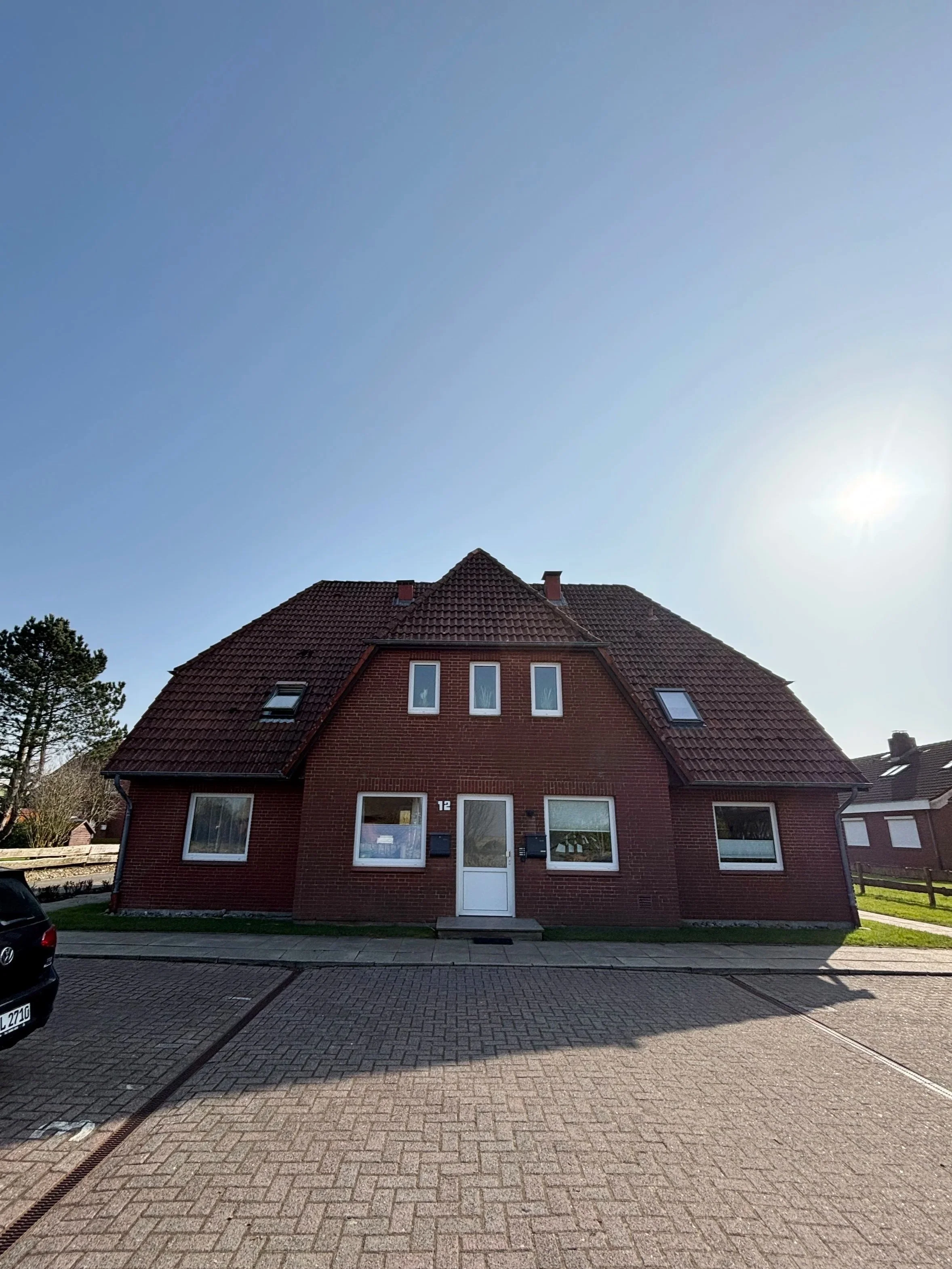 ein rotes Mehrfamilienhaus mit einem roten Ziegeldach und mehreren Fenstern, auf einer gepflasterten Straße in Deutschland, mit einem blauen Himmel im Hintergrund