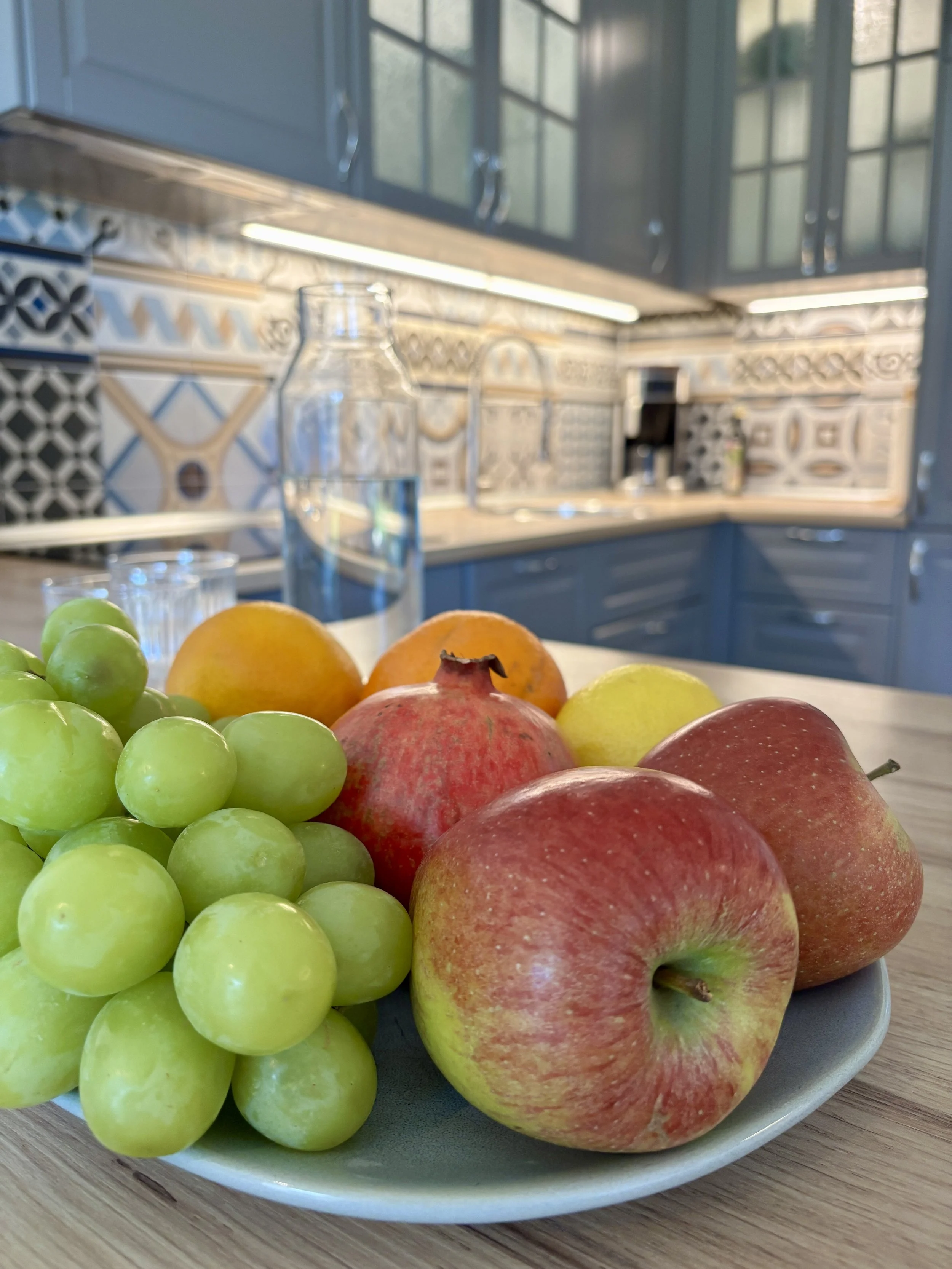 Verschiedene Früchte auf einem Teller in einer modernen Küchenumgebung mit blauen Schränken und dekorativen Keramikfliesen.