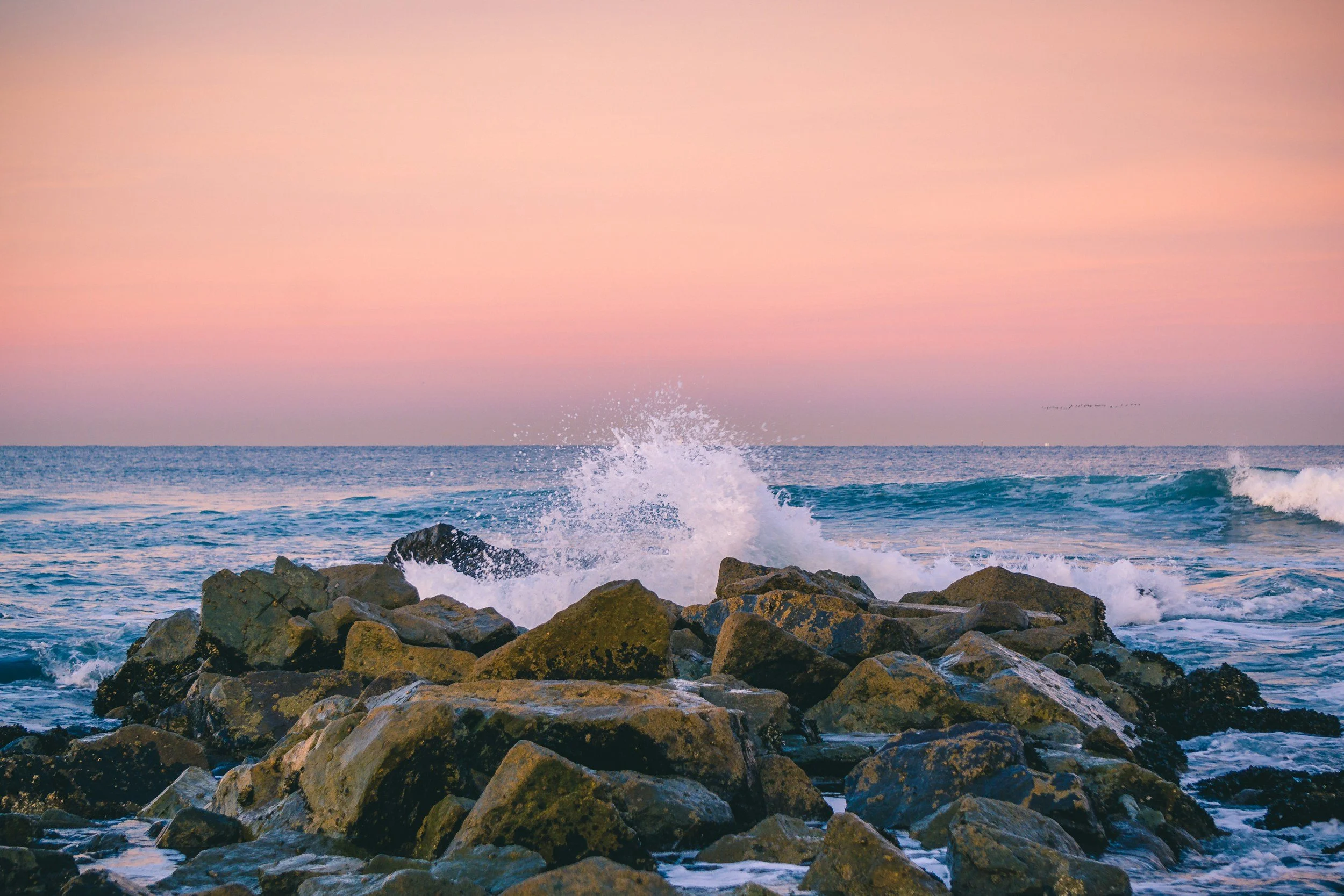 Photo showing coastal rocks with waves crashing up against them and a smooth water surface on the horizon. Representing anxiety, low mood, depression and frustration that often comes with chronic pain, heart disease or cancer diagnosis