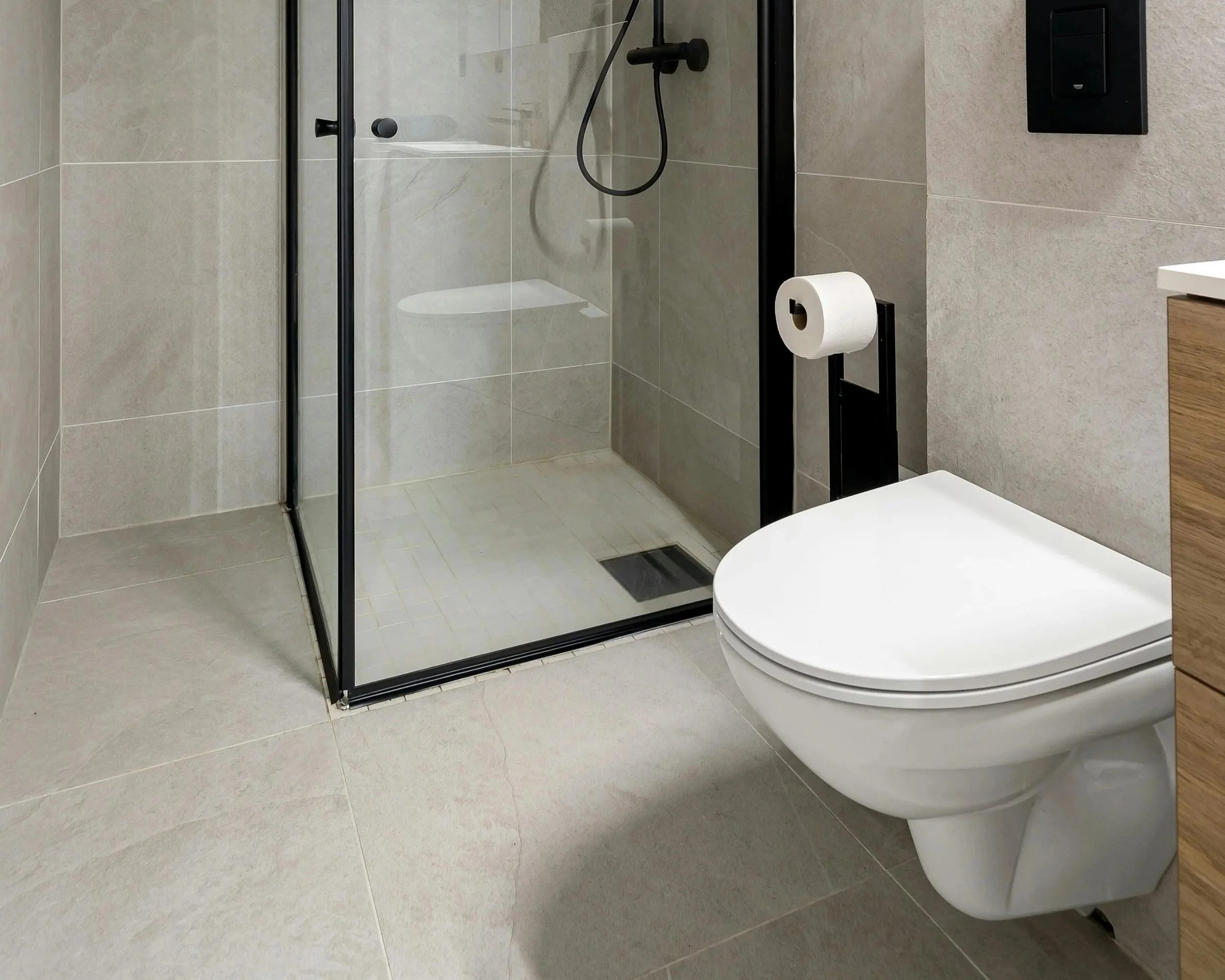 Badkamer met glazen douchecabine, toilet en een houten kast.